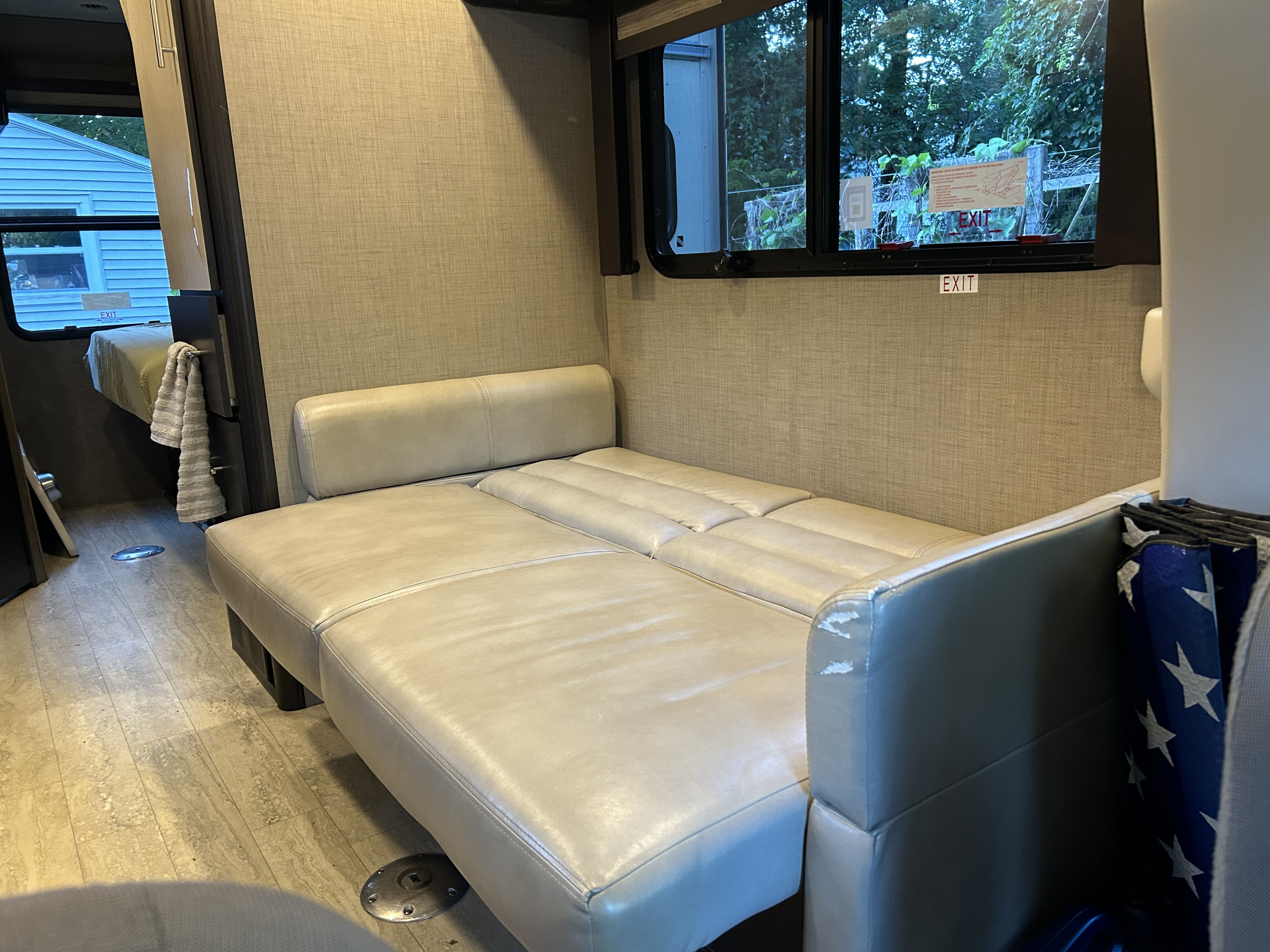 RV rental interior features a beige convertible sofa/bed, compact living space, and window with an 'EXIT' sign.. Thor Gemini 2017