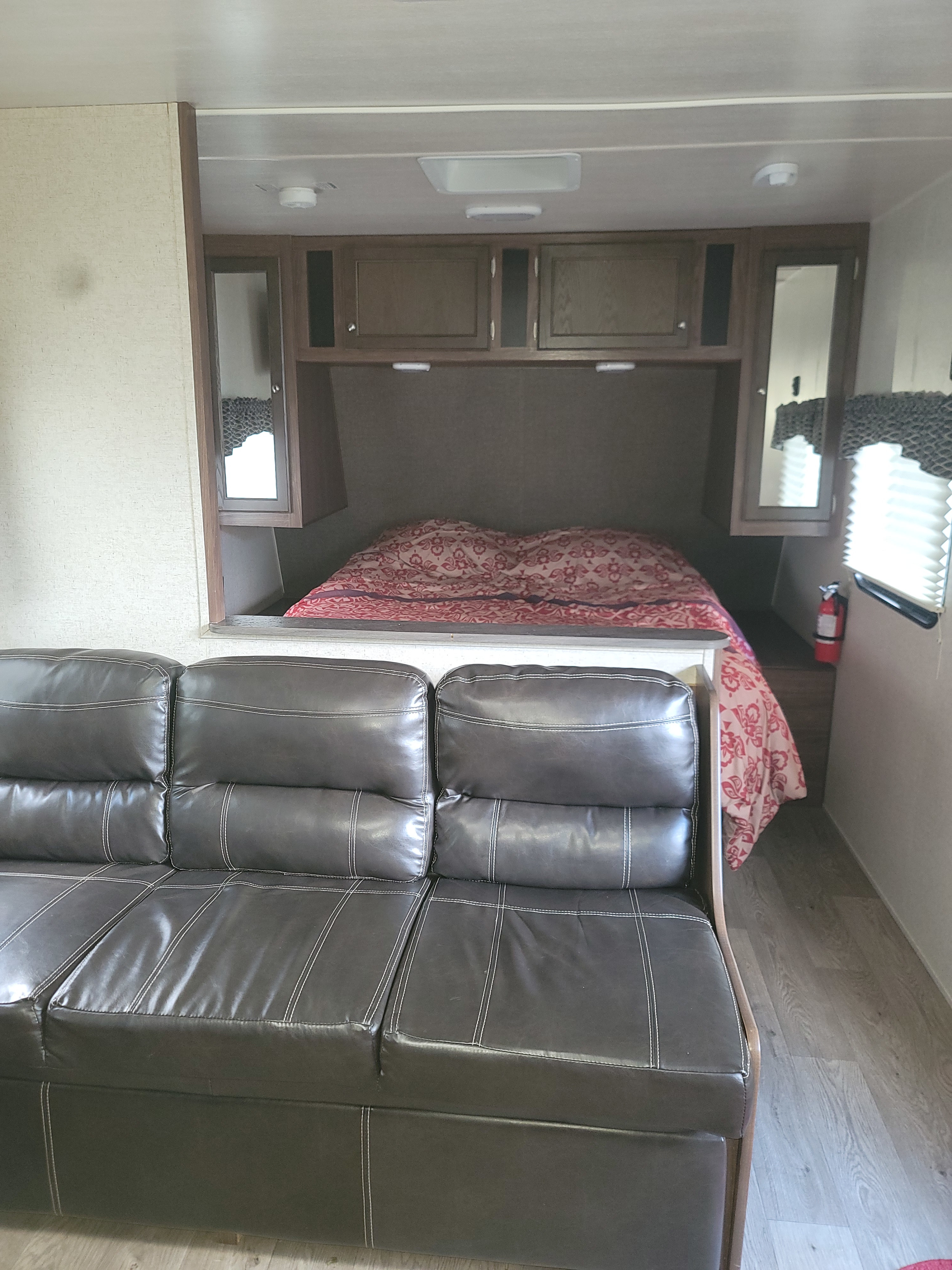 Comfortable RV rental interior featuring a dark brown sofa in the foreground and a cozy bed area with overhead storage in the back.. Heartland RVs Prowler 2018