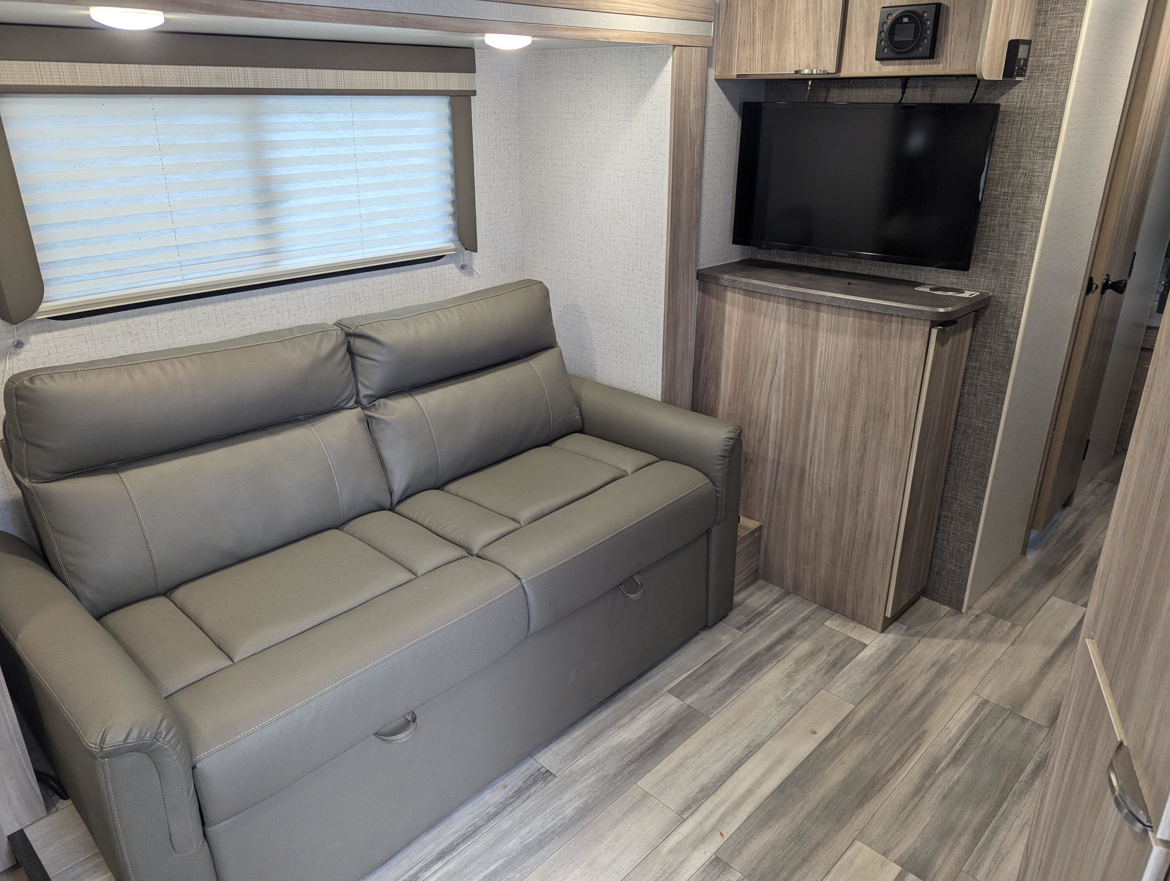 Modern RV living space with a pull-out gray sofa, TV area, and light wood finishes. Great for your next rv rental!. Winnebago Industries Towables Micro Minnie 2225RL 2022