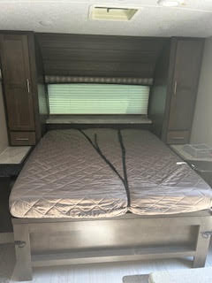 RV rental bedroom with a brown quilted bed, dark wood cabinets, and window. Perfect for your comfortable travels.. Forest River Flagstaff Micro Lite 2020