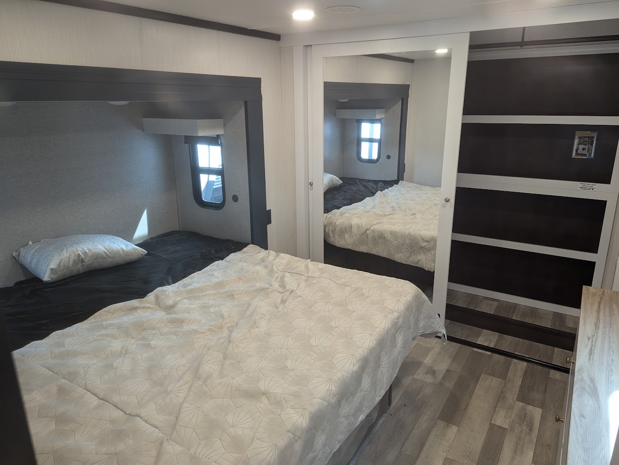 Interior of an RV rental bedroom showing a main bed, an elevated bunk, and a mirrored wardrobe. Compact comfort for trips.. Forest River Cedar Creek 2024