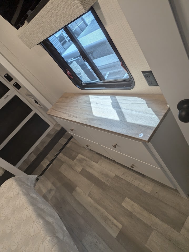 Step inside a modern RV rental bedroom. Features include a light wood dresser with four drawers, a large window, and durable wood-look flooring.. Forest River Cedar Creek 2024