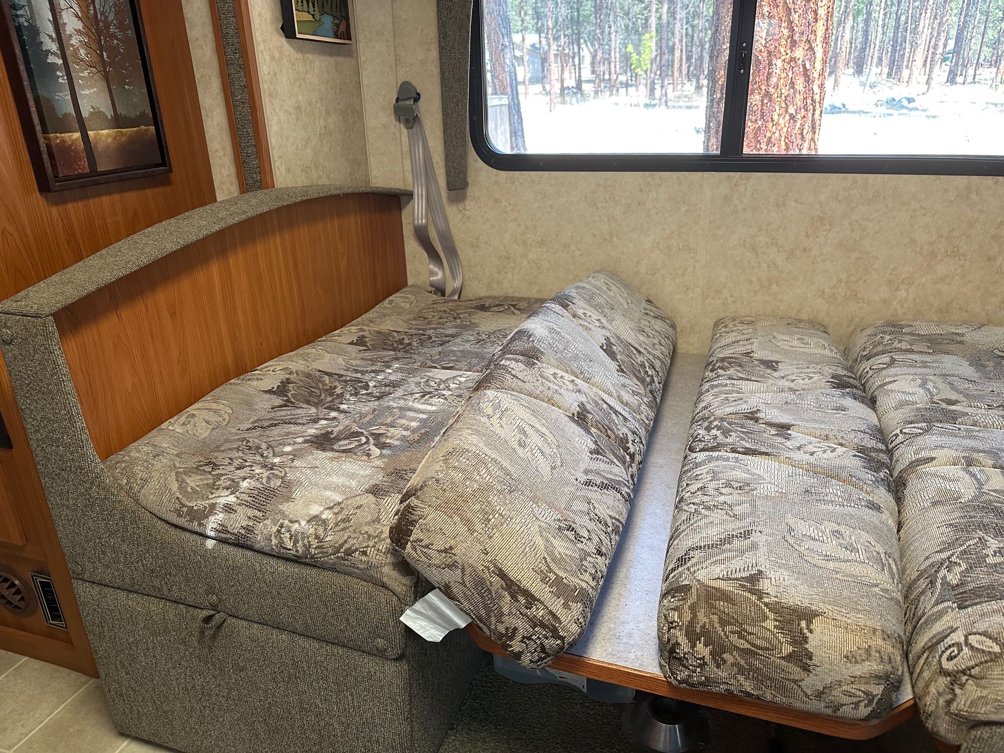 This RV rental features a flexible dinette with patterned cushions, easily converting into a bed, overlooking a serene forest view.. Bigfoot RV MH27 2006