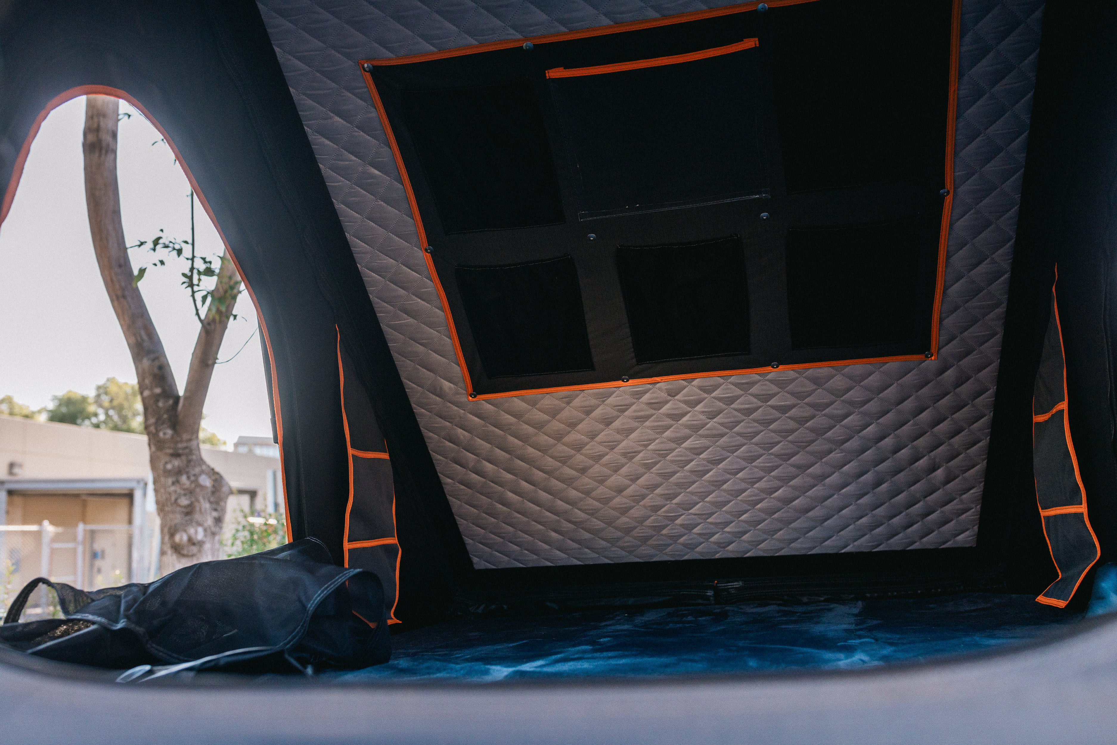 Interior of an RV rental: quilted walls, storage pockets, and a sleeping area with a mesh bag, tree visible outside.. Lexus GX460 2010