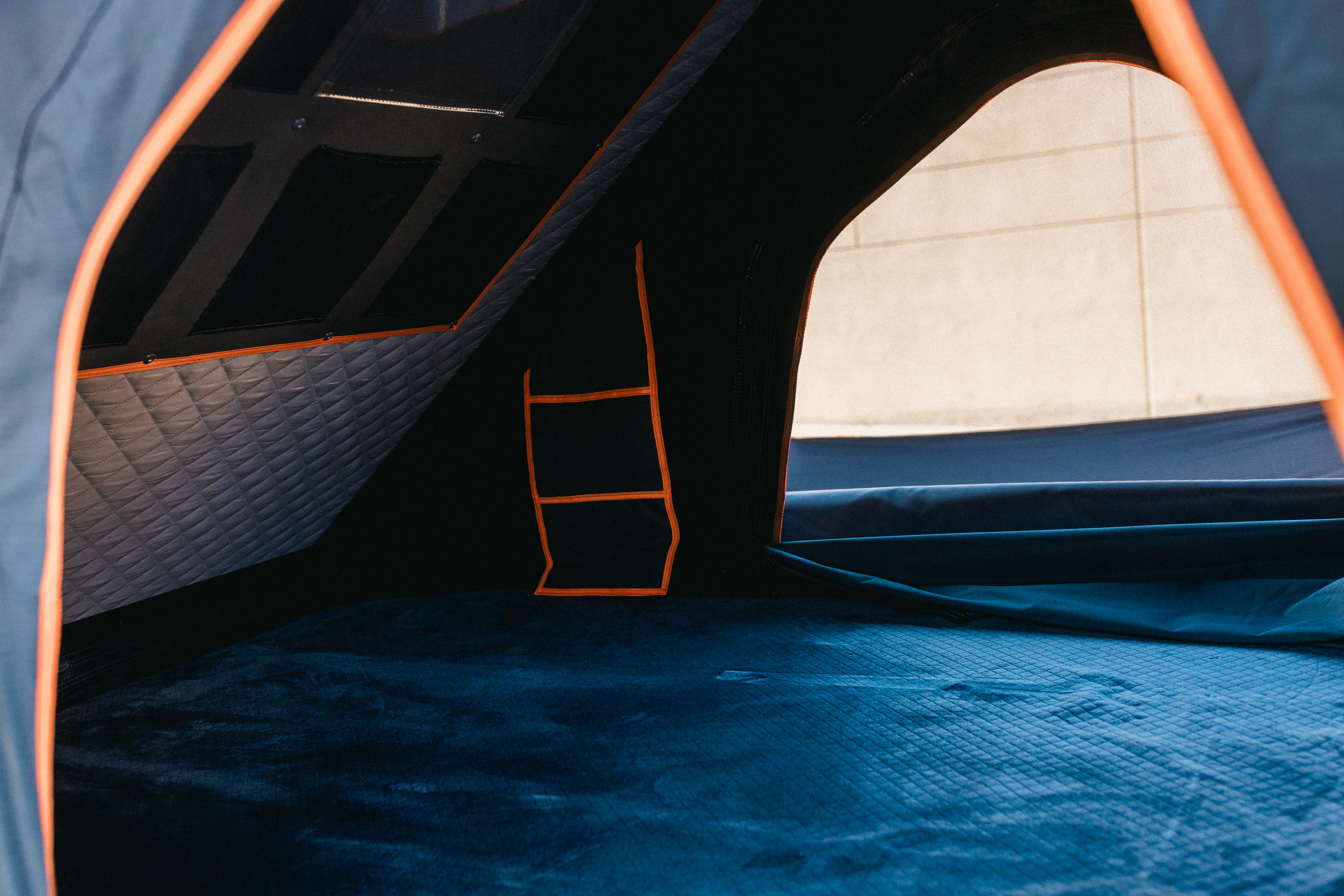 Interior of an RV rental's sleeping area, featuring a blue mattress, orange accents, and an exterior view.. Lexus GX460 2010