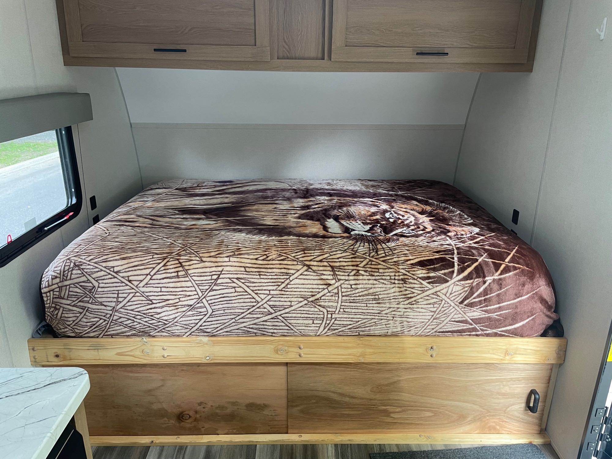 Relax in this RV rental's cozy bedroom. Features a large bed, patterned blanket, overhead cabinets, and a window.. Avenger LT 2022