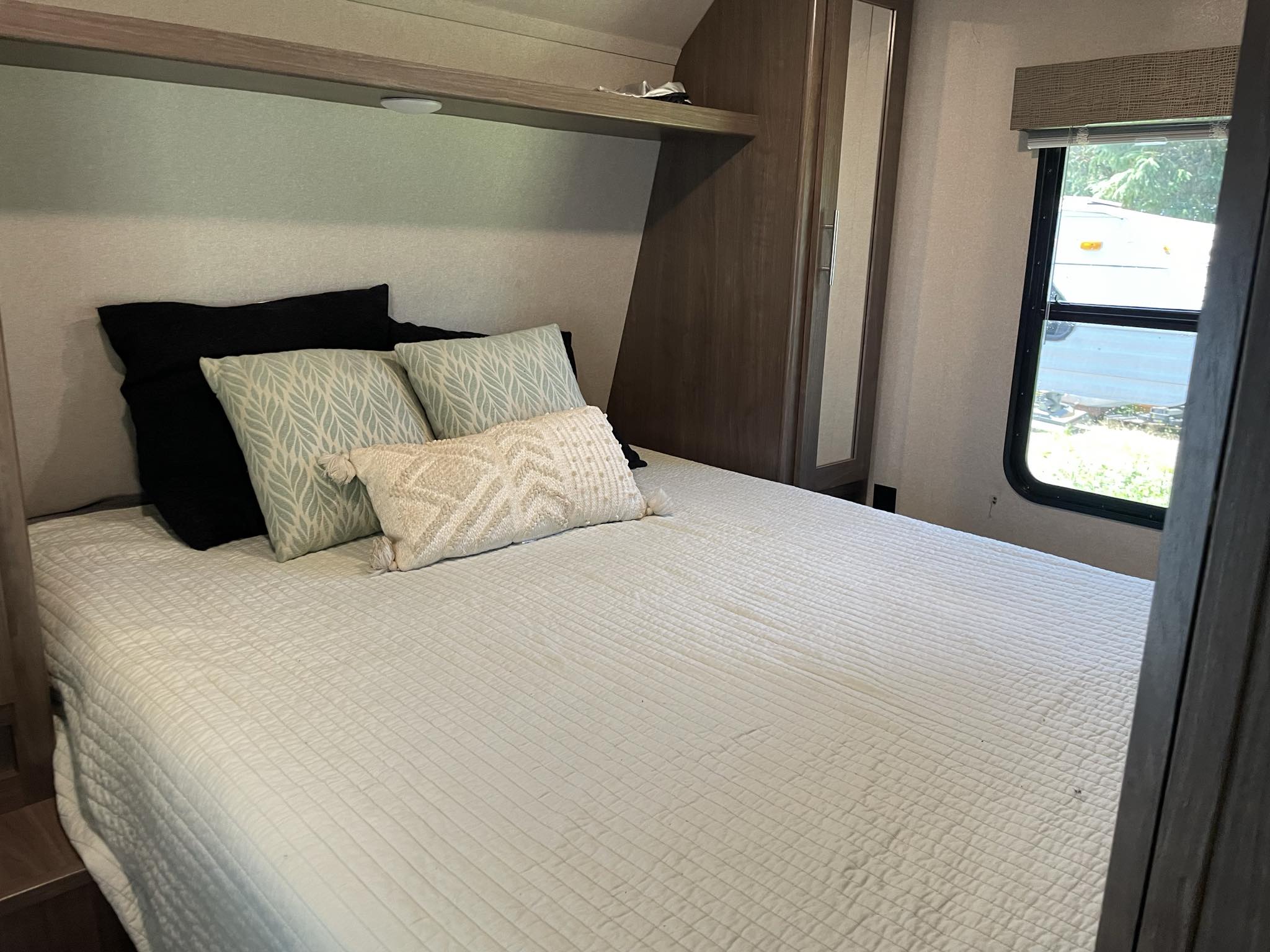 Cozy RV rental bedroom with a neatly made bed, patterned pillows, overhead shelf, and window.. Keystone RV Hideout 2019
