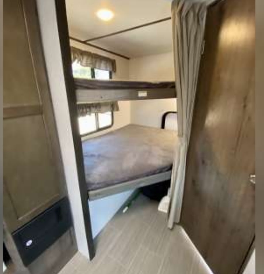 RV rental bunk beds (upper and lower) with windows and a ceiling light, offering a comfy sleeping area.. Keystone RV Passport SL 2021