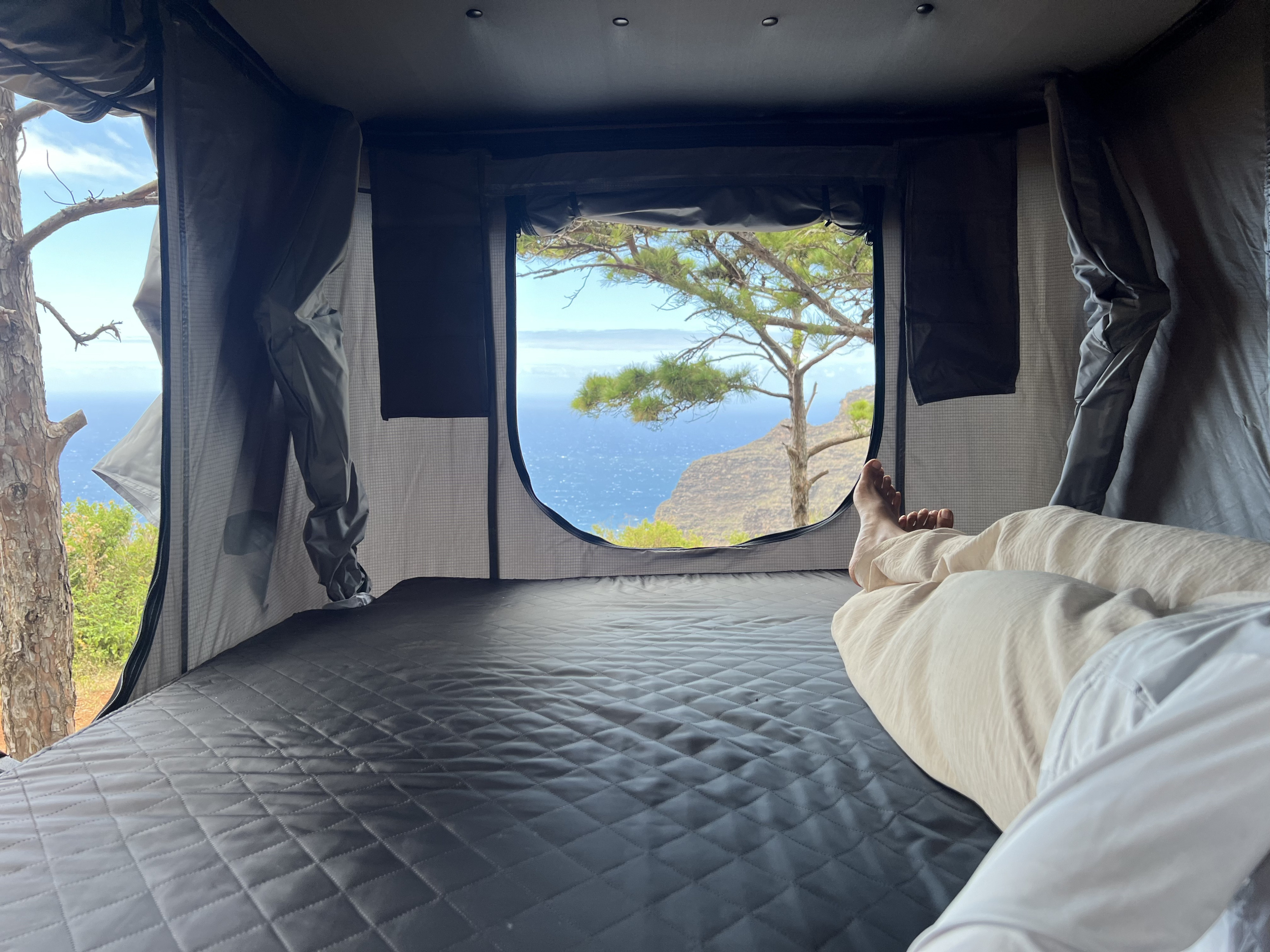Relaxing in an RV rental's cozy rooftop tent, offering stunning ocean and cliff views. A perfect nature escape.. Jeep Wrangler 2008