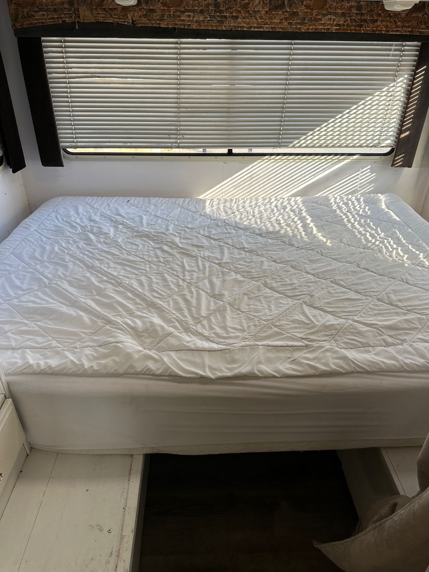 Bright RV rental bedroom with a white bed and striped sunlight filtering through horizontal window blinds.. Fleetwood Tioga 1994