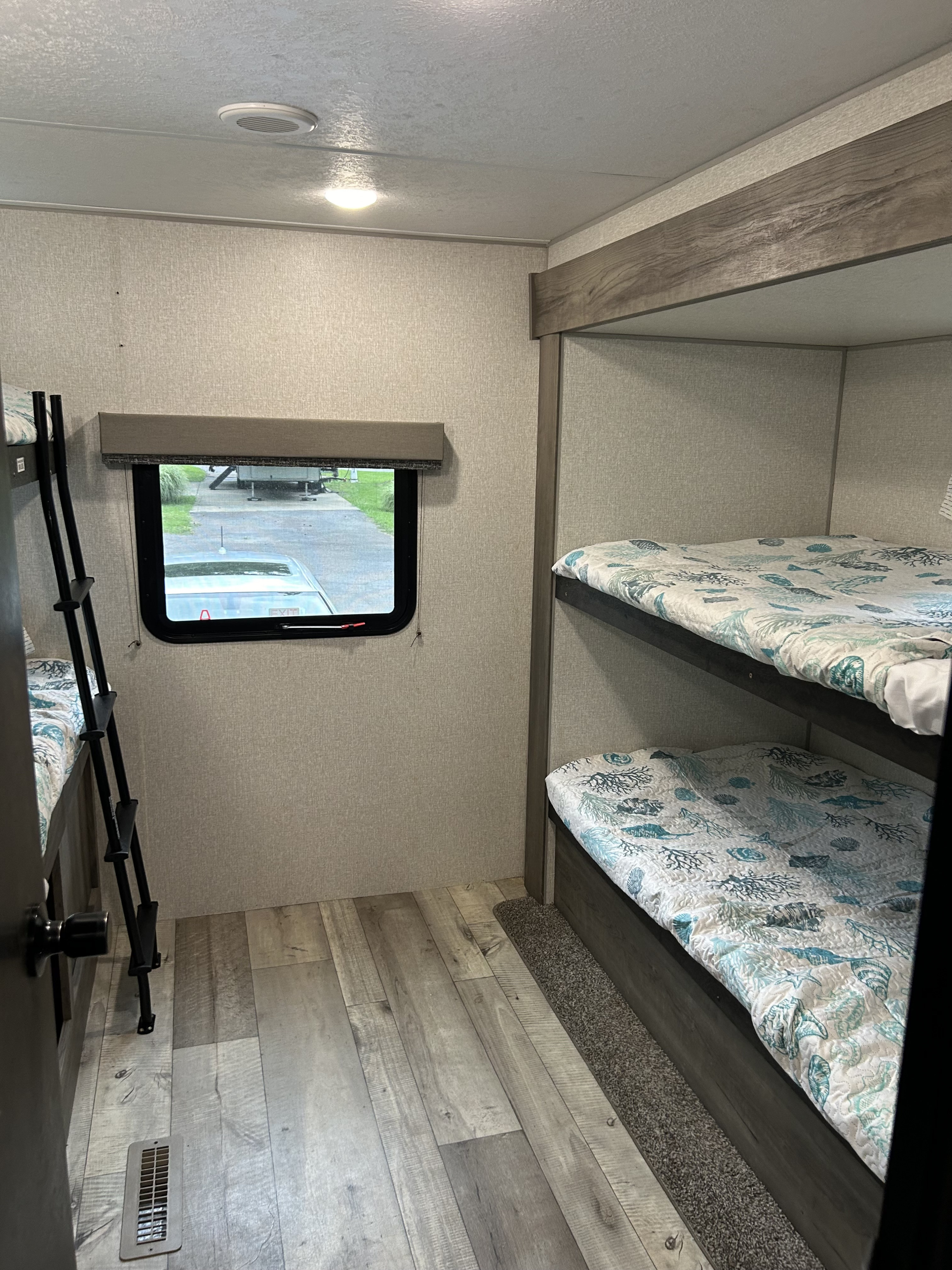 An RV rental interior featuring twin bunk beds with ocean-themed bedding, a small window, and light wood flooring.. KZ Sportsmen 2021