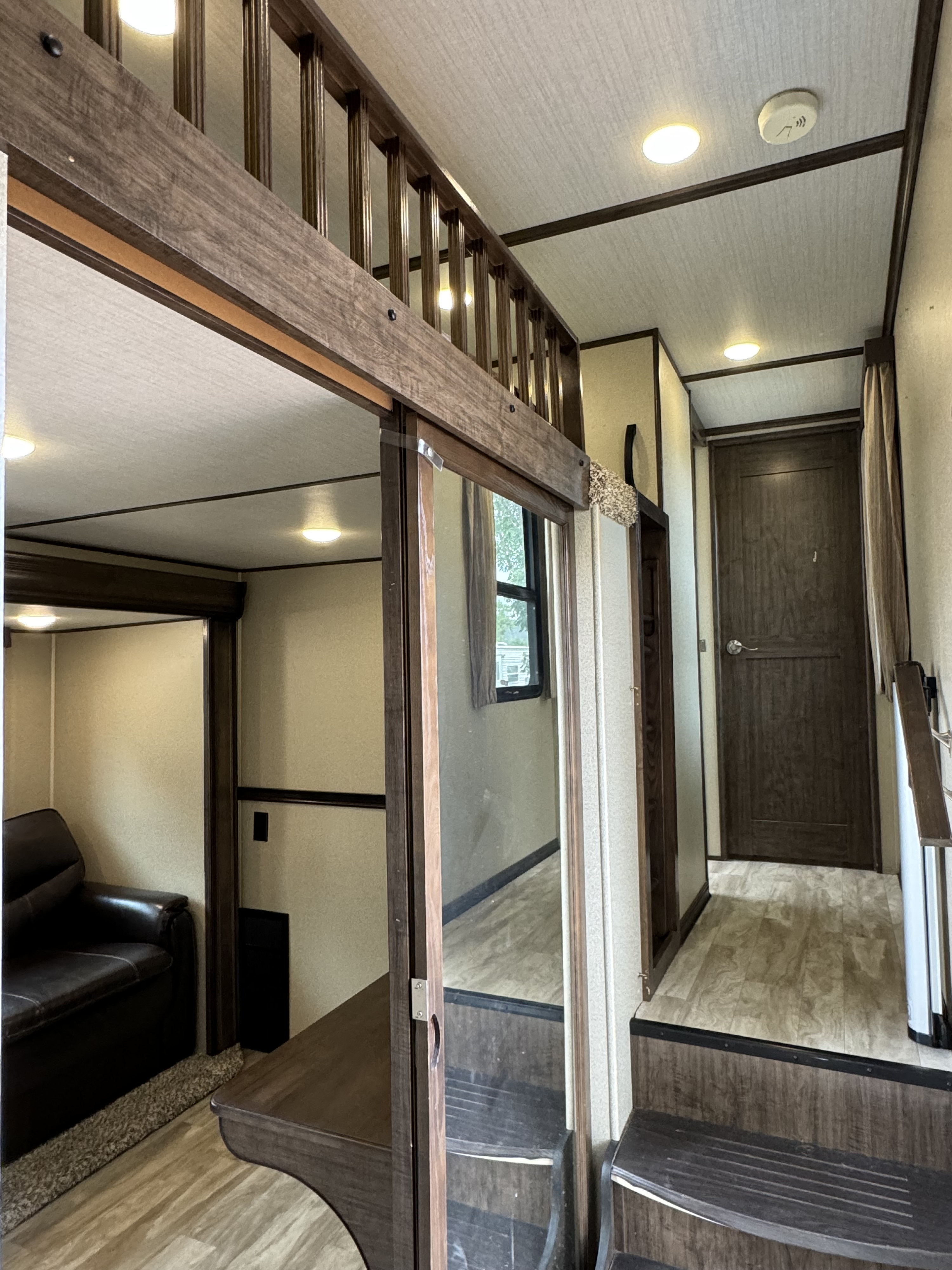 RV rental's inviting interior, featuring a cozy living area, stairs to a loft, and a well-lit hallway with a dark wood door.. Grand Design Solitude 2018