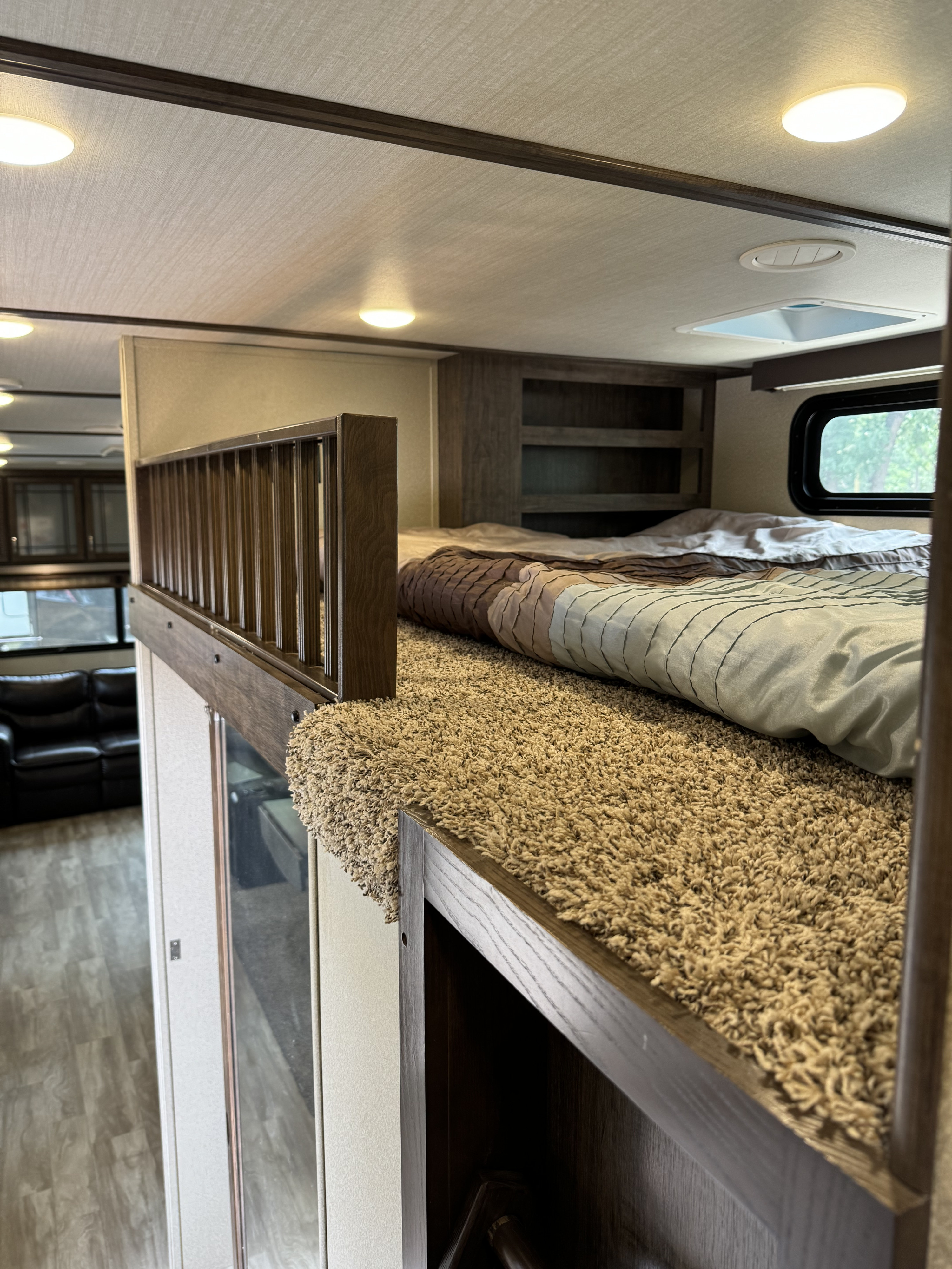This RV rental offers a cozy loft bedroom with a textured comforter, plush shag carpet, and wooden railing.. Grand Design Solitude 2018