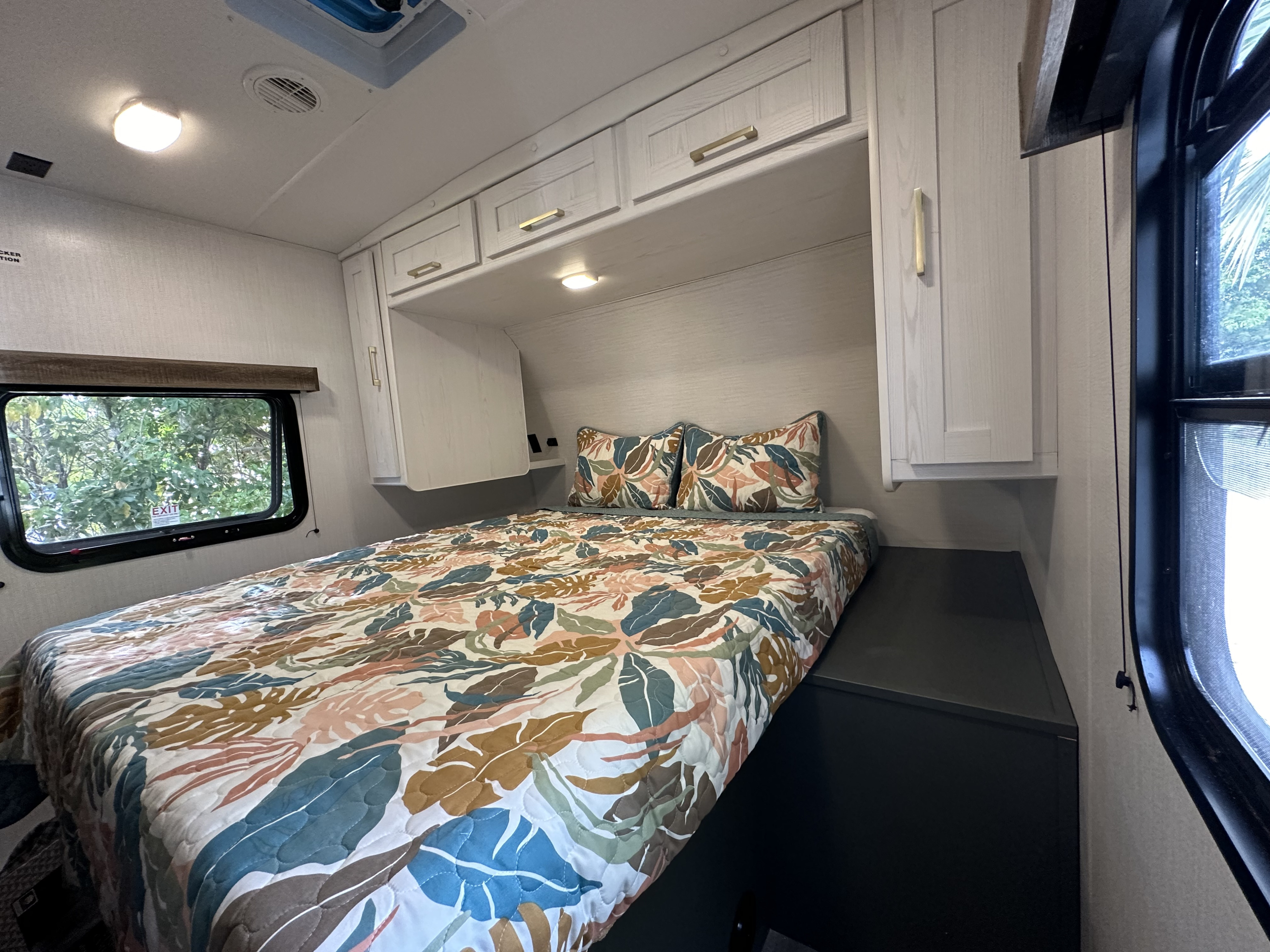 Experience comfort in this RV rental bedroom: features a bright patterned comforter, overhead cabinets, and window.. Heartland RVs Eddie Bauer Rear bunkhouse with front bedroom 2024