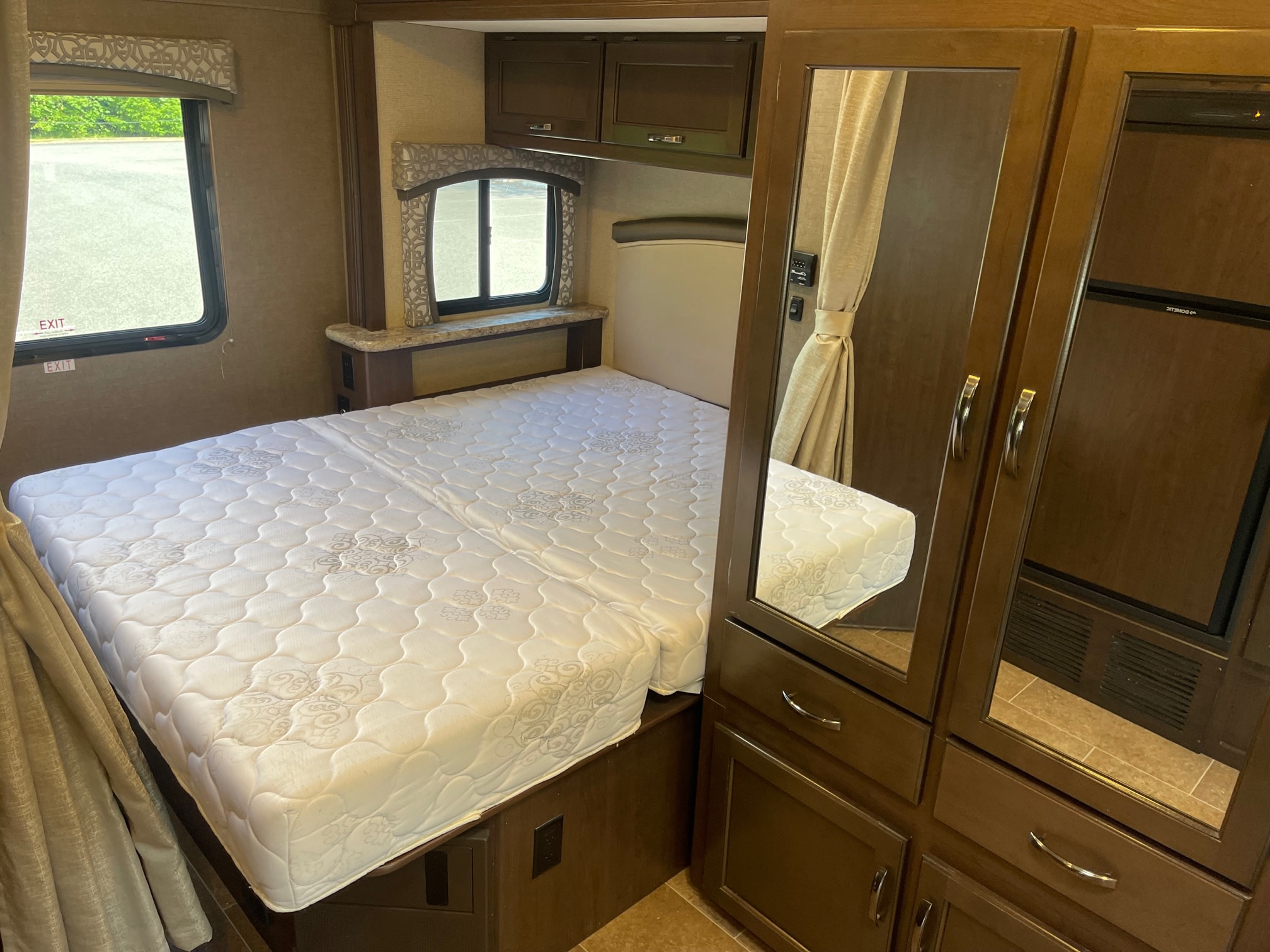 Clean RV rental bedroom with white bed, mirrored closet, overhead cabinets, and window. Ideal for cozy travels.. Thor Chateau 2019