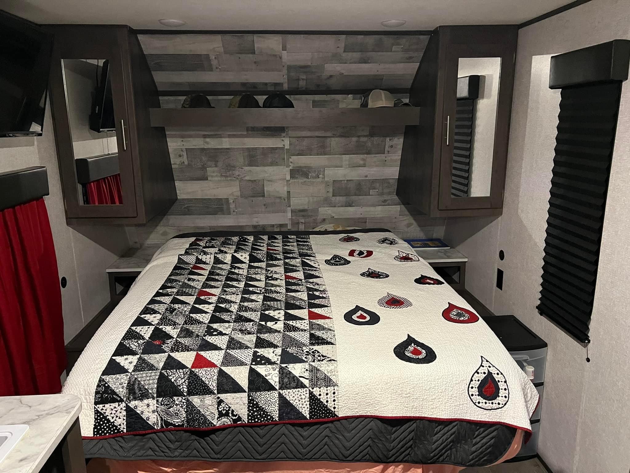 This cozy RV rental bedroom features a unique quilt, overhead cabinets, and blackout blinds for your comfort.. Dutchmen Coleman Lantern LT 2021
