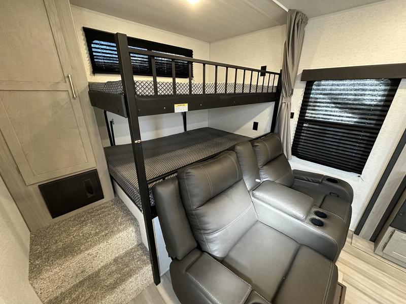 RV rental interior: grey recliners face bunk beds on a raised platform, with steps and cabinet to the left.. Keystone RV Springdale 2024