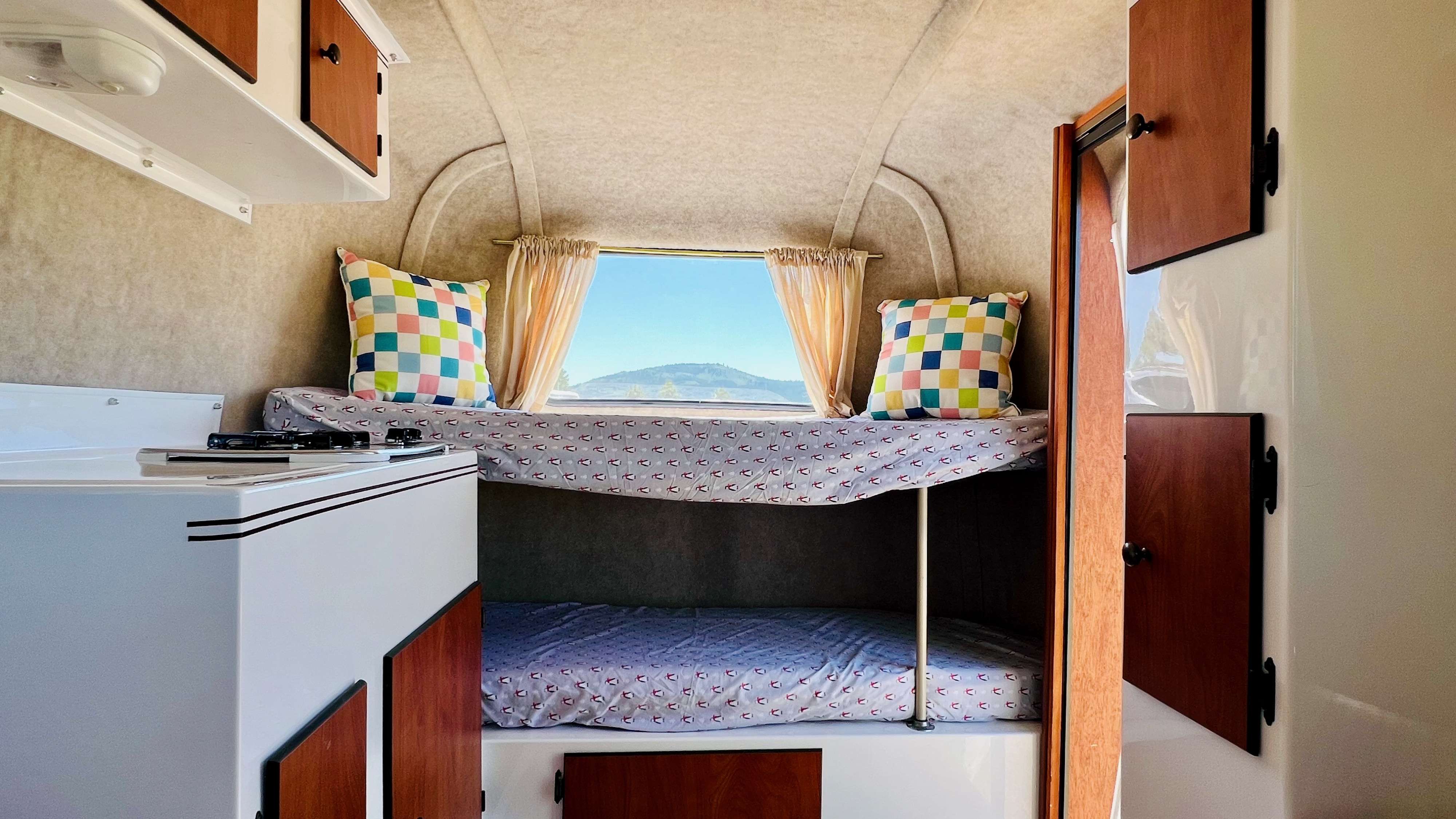 Cozy RV rental interior with bunk beds, a kitchen counter, and a window showcasing a mountain view.. Scamp Scamp Trailer 2015