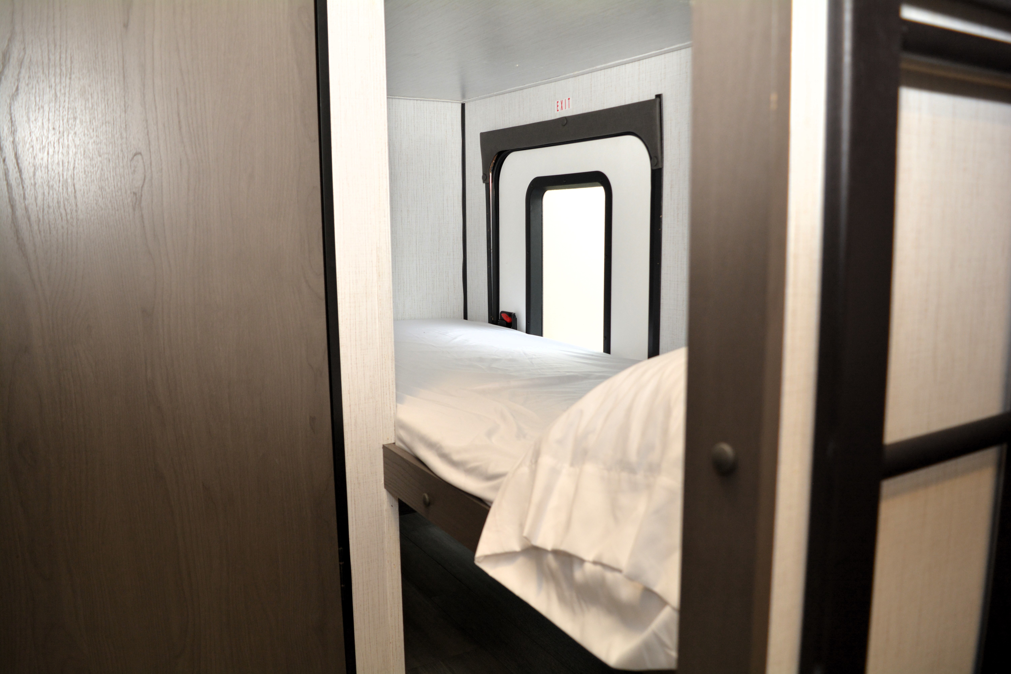 Compact RV rental sleeping area featuring a bunk bed with white bedding and a visible exit door.. Heartland RVs Mallard Pathfinder 2022