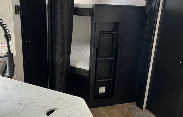 RV rental interior shows a dark bunk bed sleeping area with ladder and storage, next to a white countertop.. Forest River Cherokee 2022