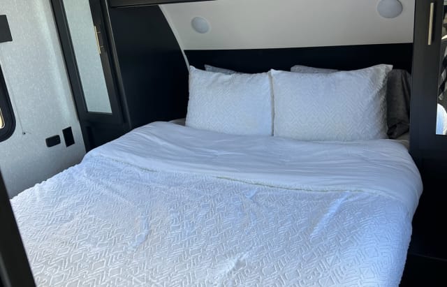 Cozy RV rental bedroom with pristine white bedding & dark accents. Perfect for a comfortable travel journey.. Forest River Cherokee 2022