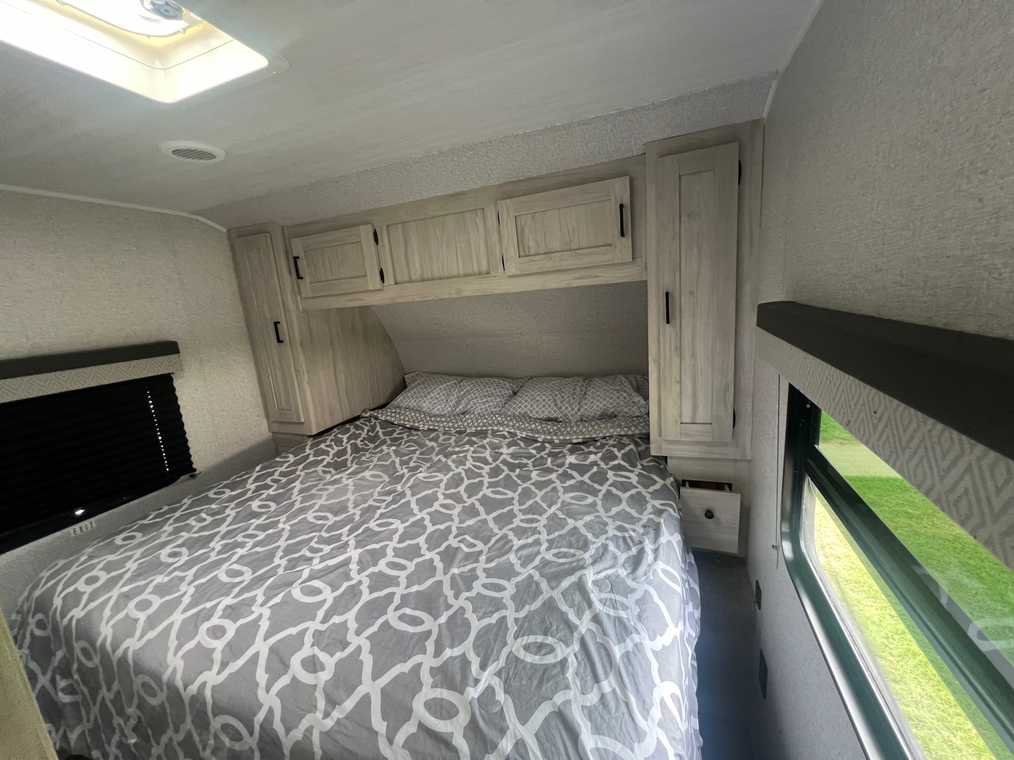 Cozy RV rental bedroom with patterned bed, cabinets, and a window view. Perfect for travel accommodations.. East to West Della Terra 2022