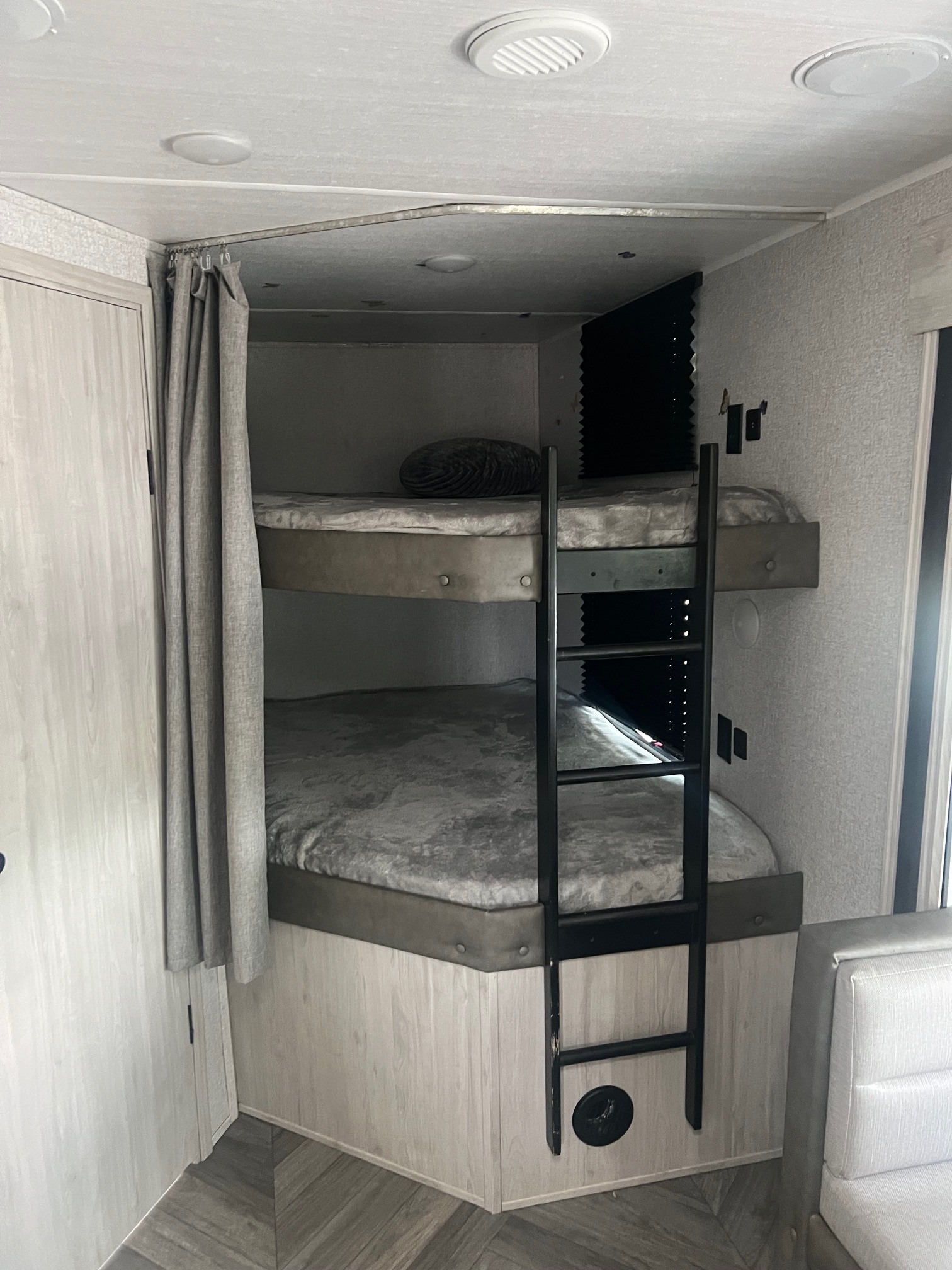 RV rental interior: two grey bunk beds with a ladder and curtain, designed for efficient sleeping in a compact space.. East to West Della Terra 2022