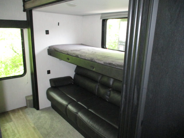 This RV rental's interior features a dark sofa below a suspended bunk bed, offering efficient sleeping arrangements.. Forest River Cherokee 304BH 2022