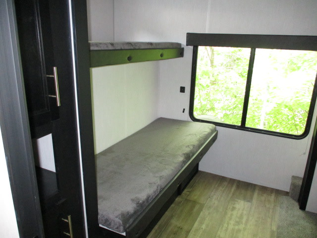 Experience comfort in this RV rental bunk area, featuring a lower and upper bed, and a large window overlooking nature.. Forest River Cherokee 304BH 2022