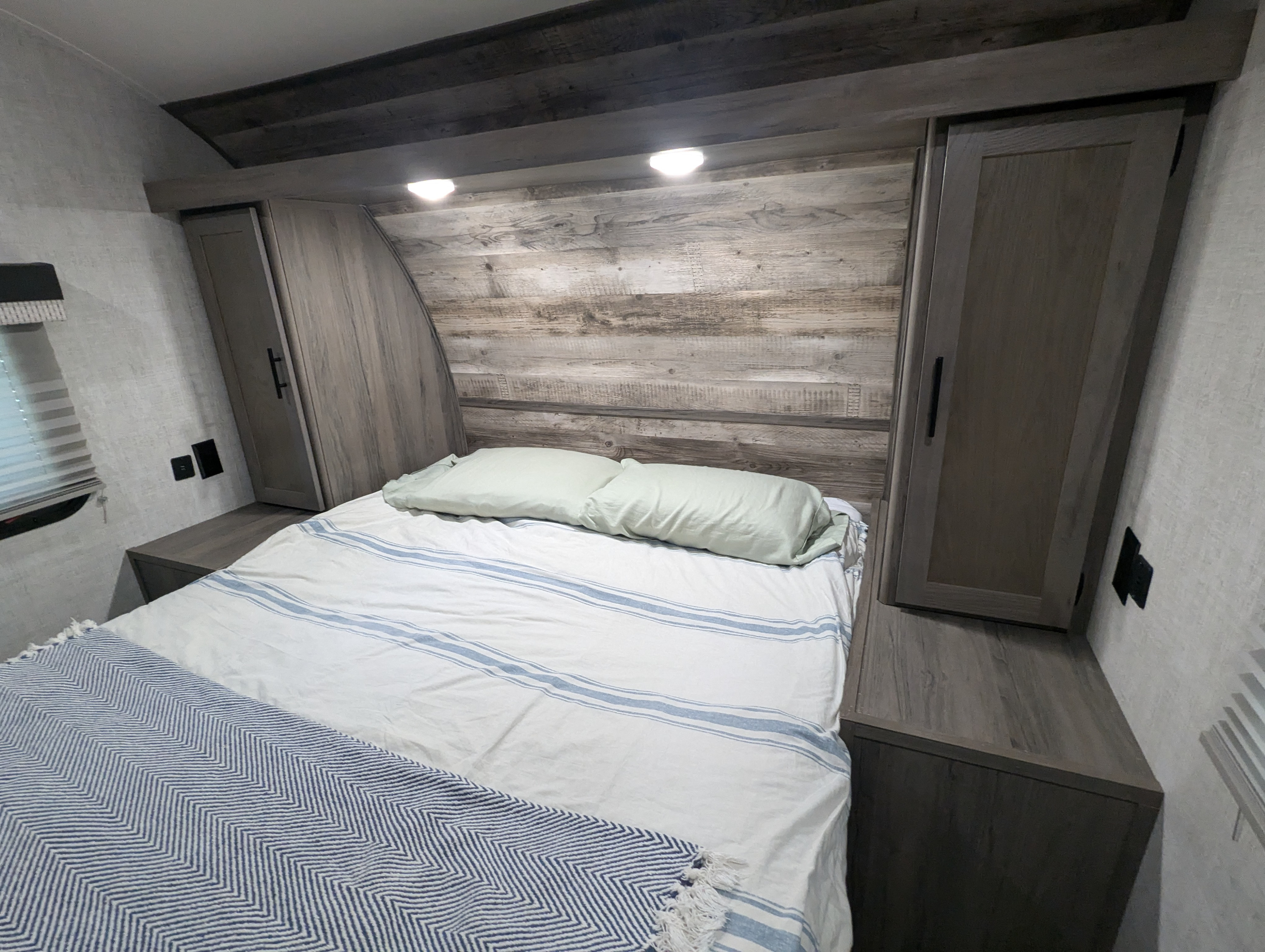 Cozy bedroom interior in an RV rental, featuring a bed with striped bedding, rustic headboard, and storage cabinets.. Gulf Stream Enlighten 2021