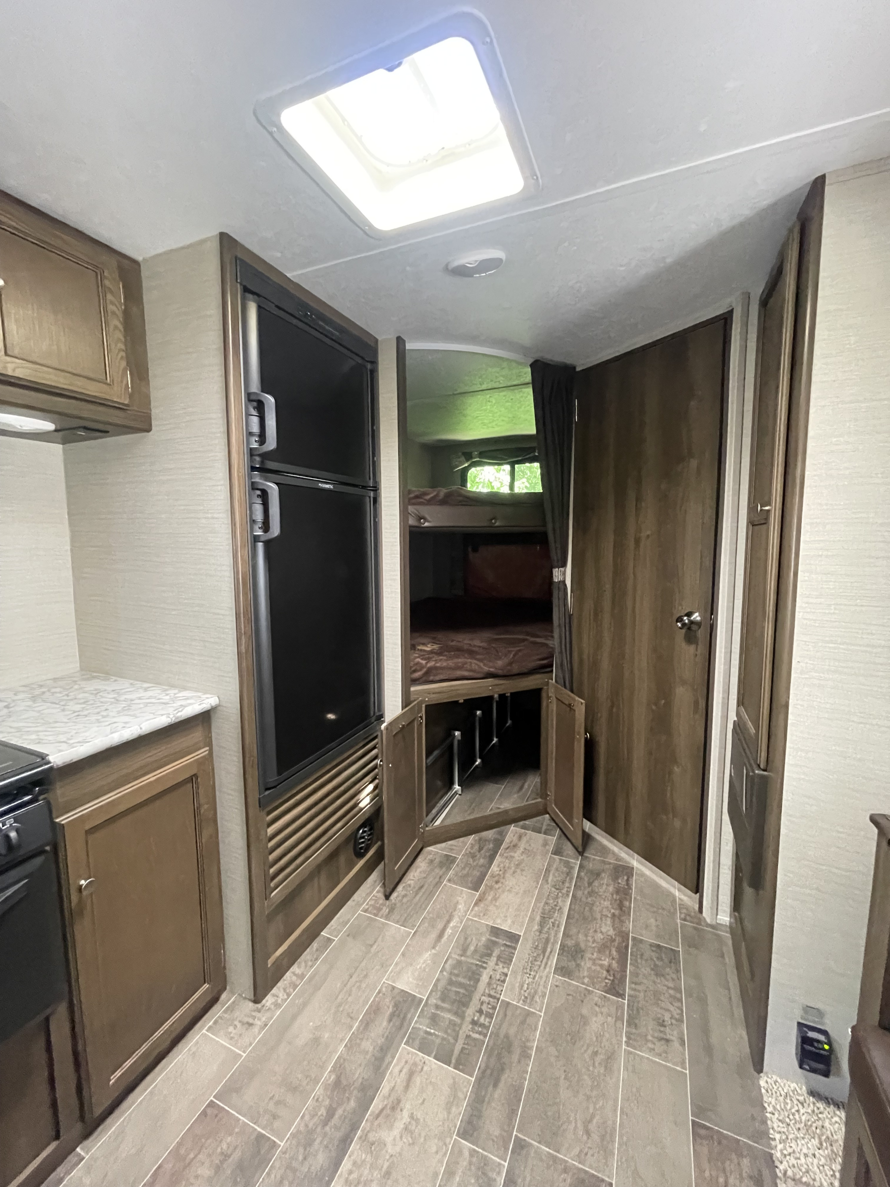 Compact RV rental interior featuring a modern kitchen, large fridge, bunks, and plank flooring, lit by a skylight.. Keystone RV Bullet Ultra Lite 2018