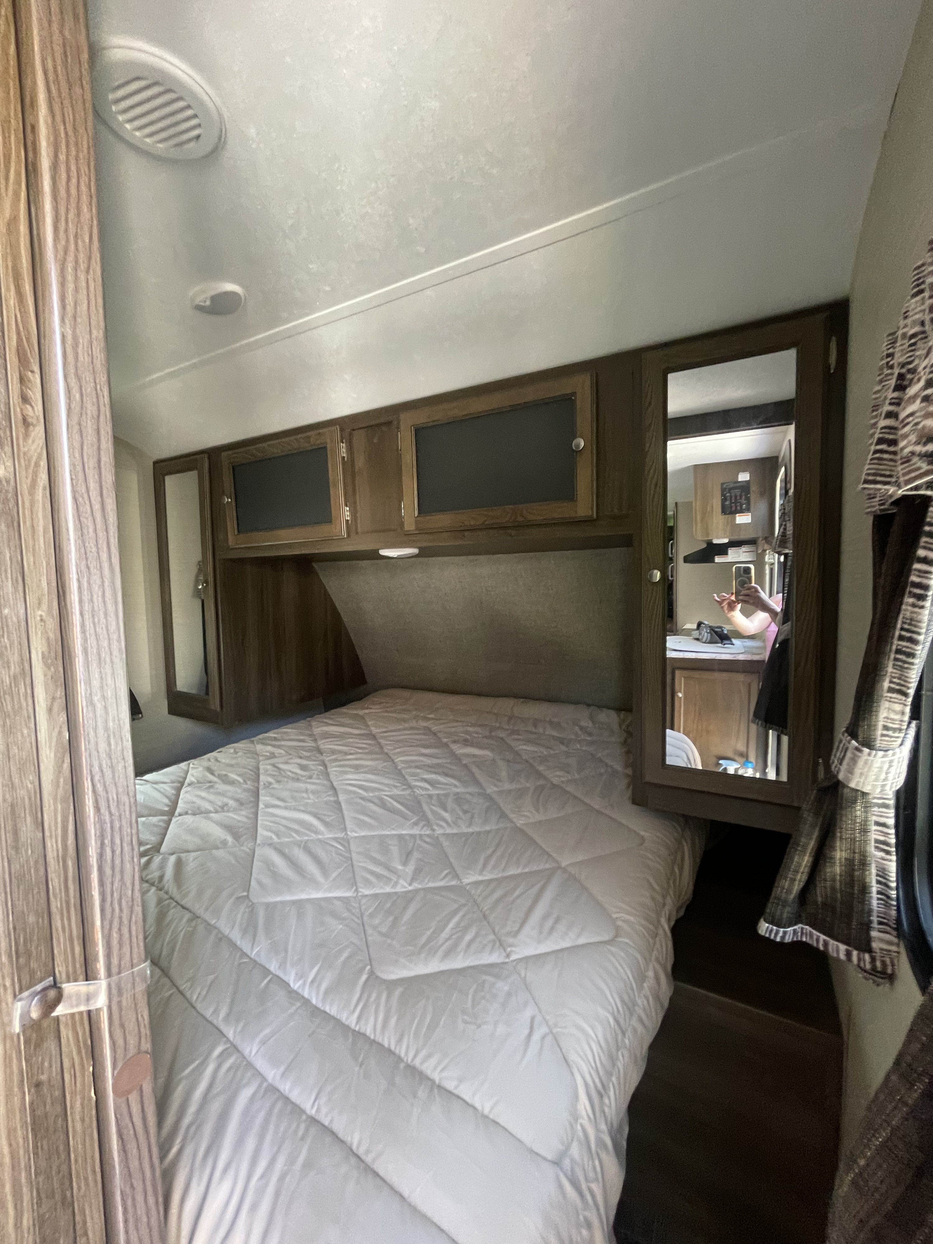 This RV rental's bedroom features a white bed, overhead cabinets, and a mirror reflecting the living space.. Keystone RV Bullet Ultra Lite 2018