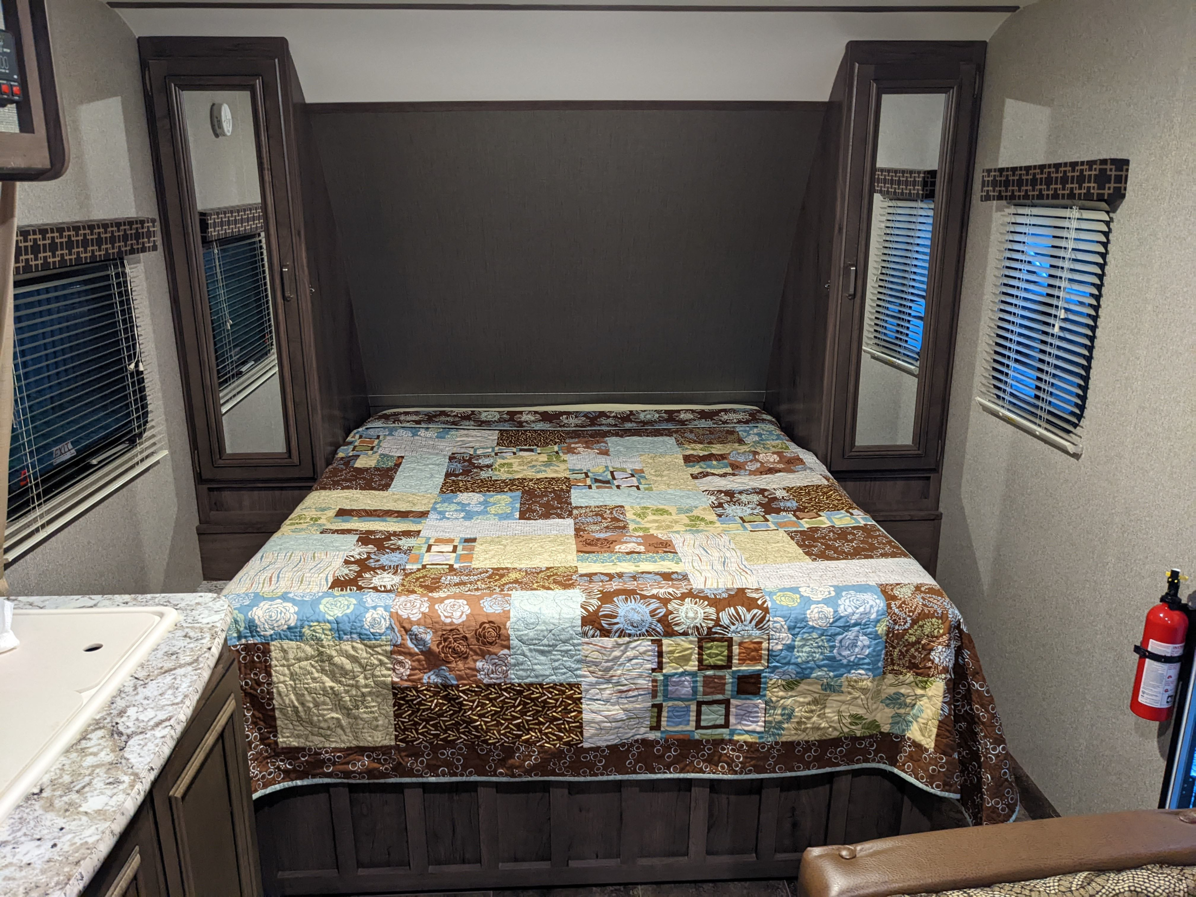 An RV rental bedroom showing a bed with a vibrant quilt, mirrored cabinets, and windows on both sides.. Keystone RV Passport Ultra Lite 2018