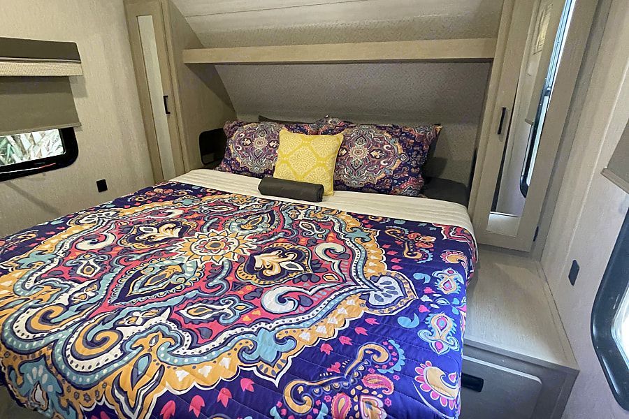 Vibrant RV rental bedroom: a cozy bed with a colorful, patterned quilt and pillows, plus built-in storage.. Forest River Salem Cruise Lite 2023