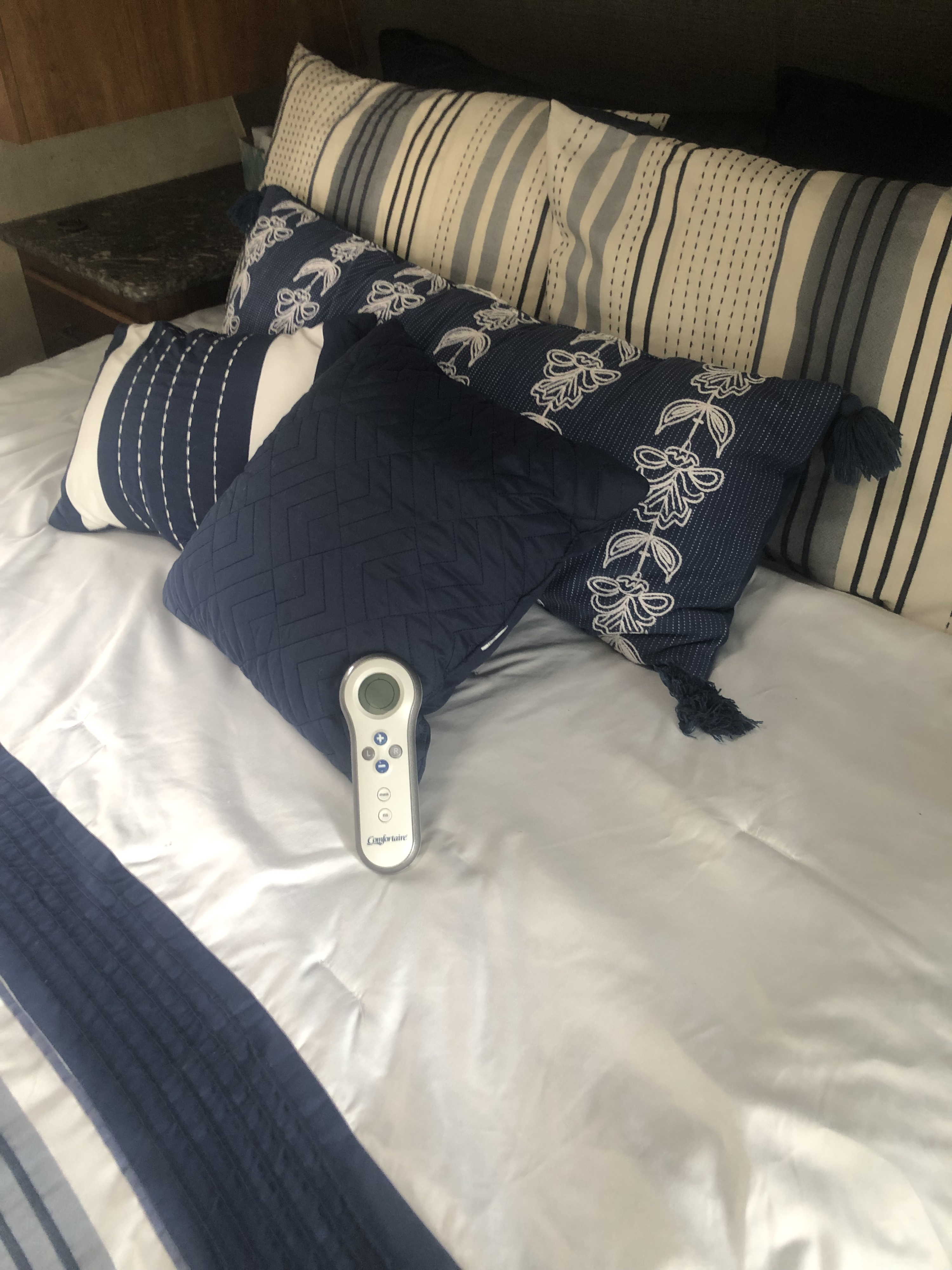 RV rental bedroom interior: neatly made bed with white sheets, blue/white decorative pillows, and a Comfortaire remote.. Keystone RV Springdale 2017