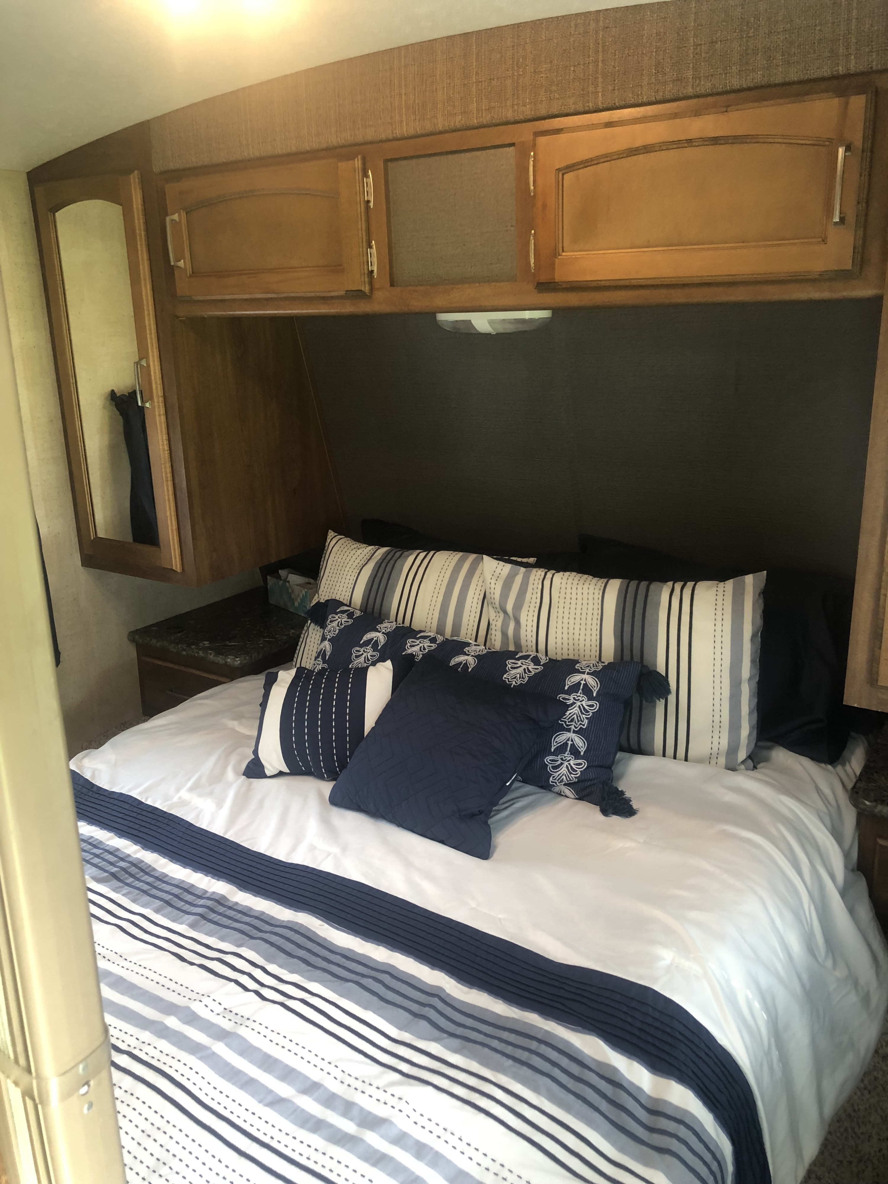 Comfortable RV rental bedroom interior featuring striped bedding, storage, and cozy overhead lighting.. Keystone RV Springdale 2017