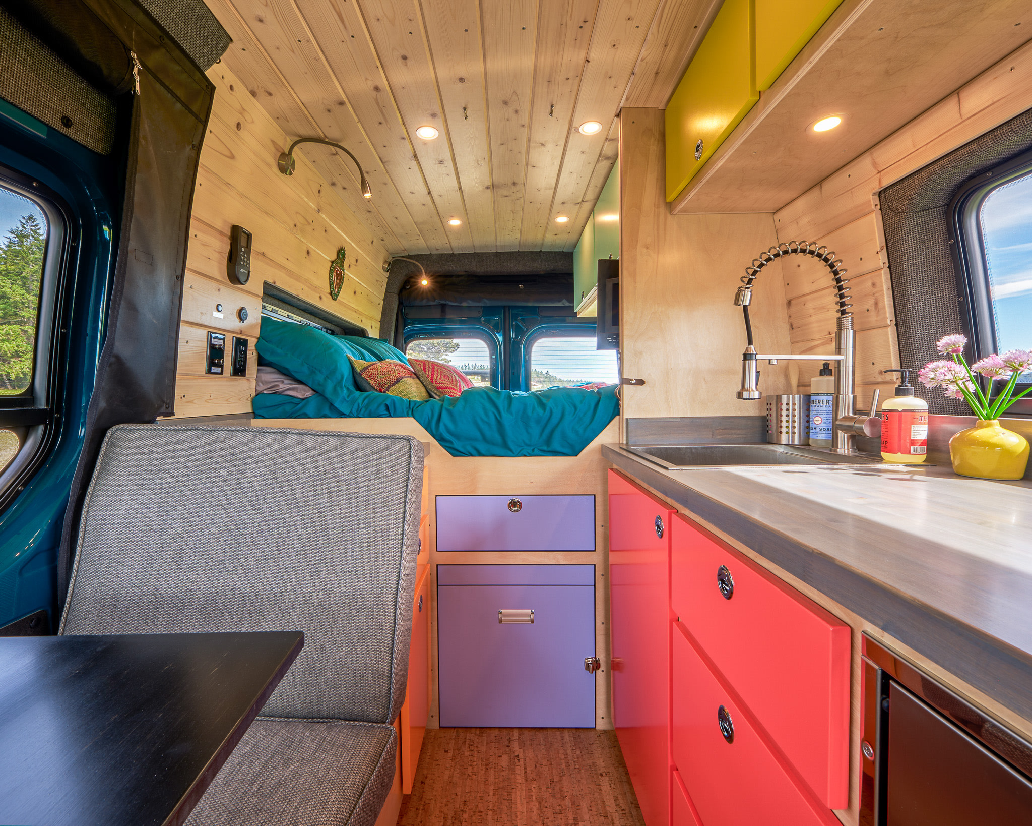 Vibrant RV rental interior: teal bed, bright kitchen with red and purple cabinets, and gray seating. Ready for adventure.. Mercedes Sprinter 2022