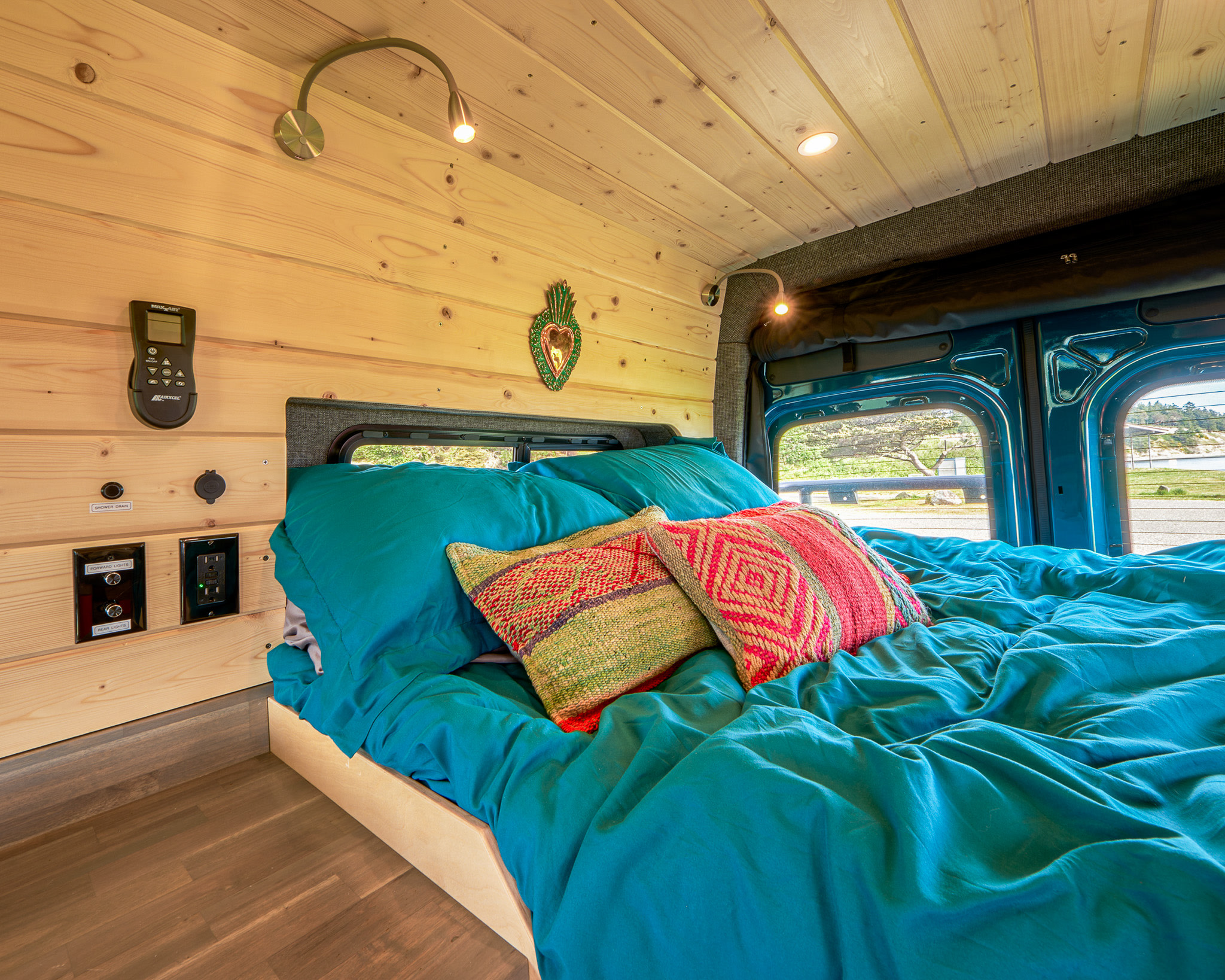 Cozy RV rental bedroom with warm wood walls, teal bedding, reading lights, and practical controls for a comfortable stay.. Mercedes Sprinter 2022