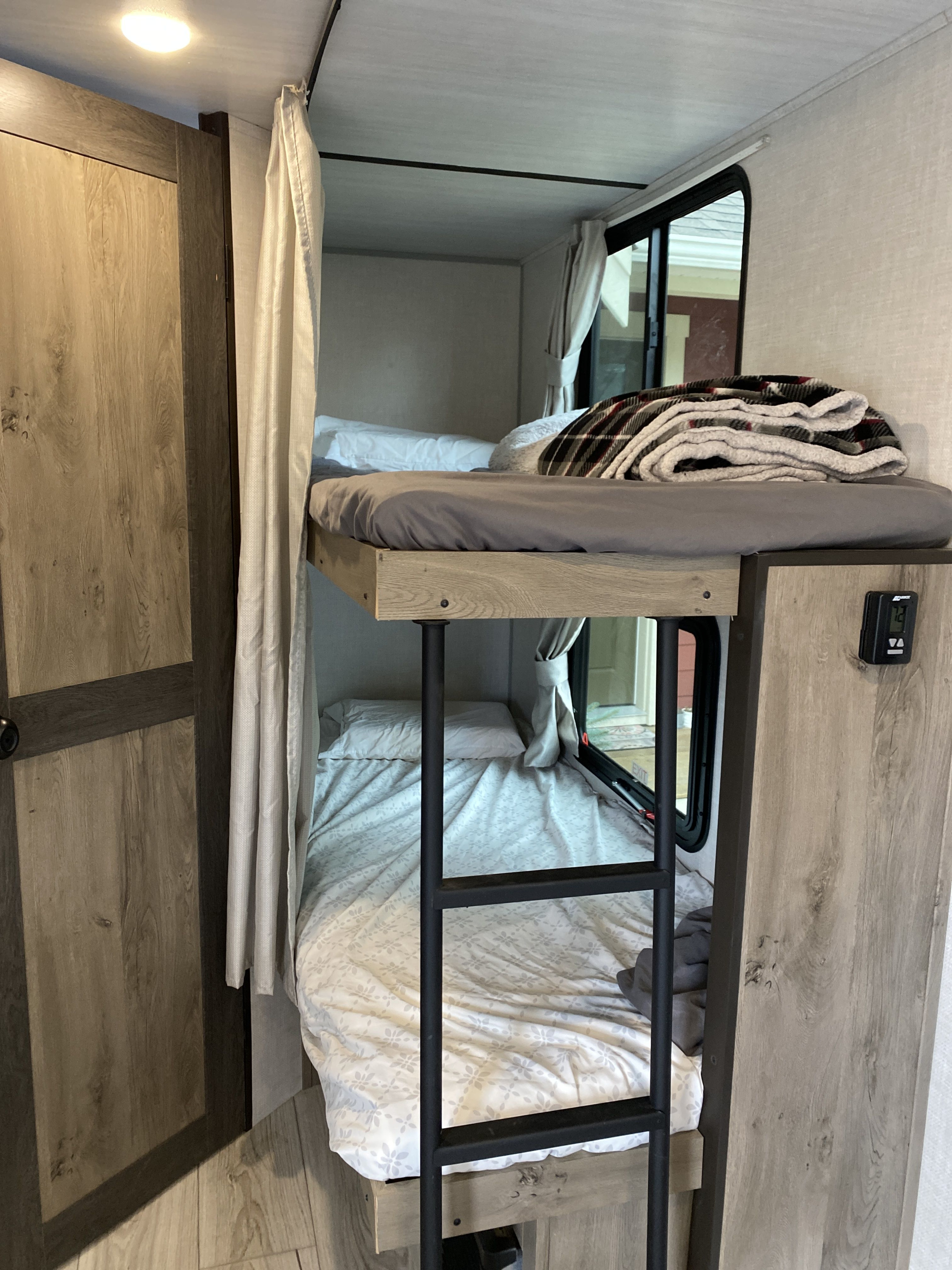 An RV rental features cozy bunk beds with a ladder, curtains, and windows, providing a compact sleeping area for travel.. Forest River Surveyor Legend 2022