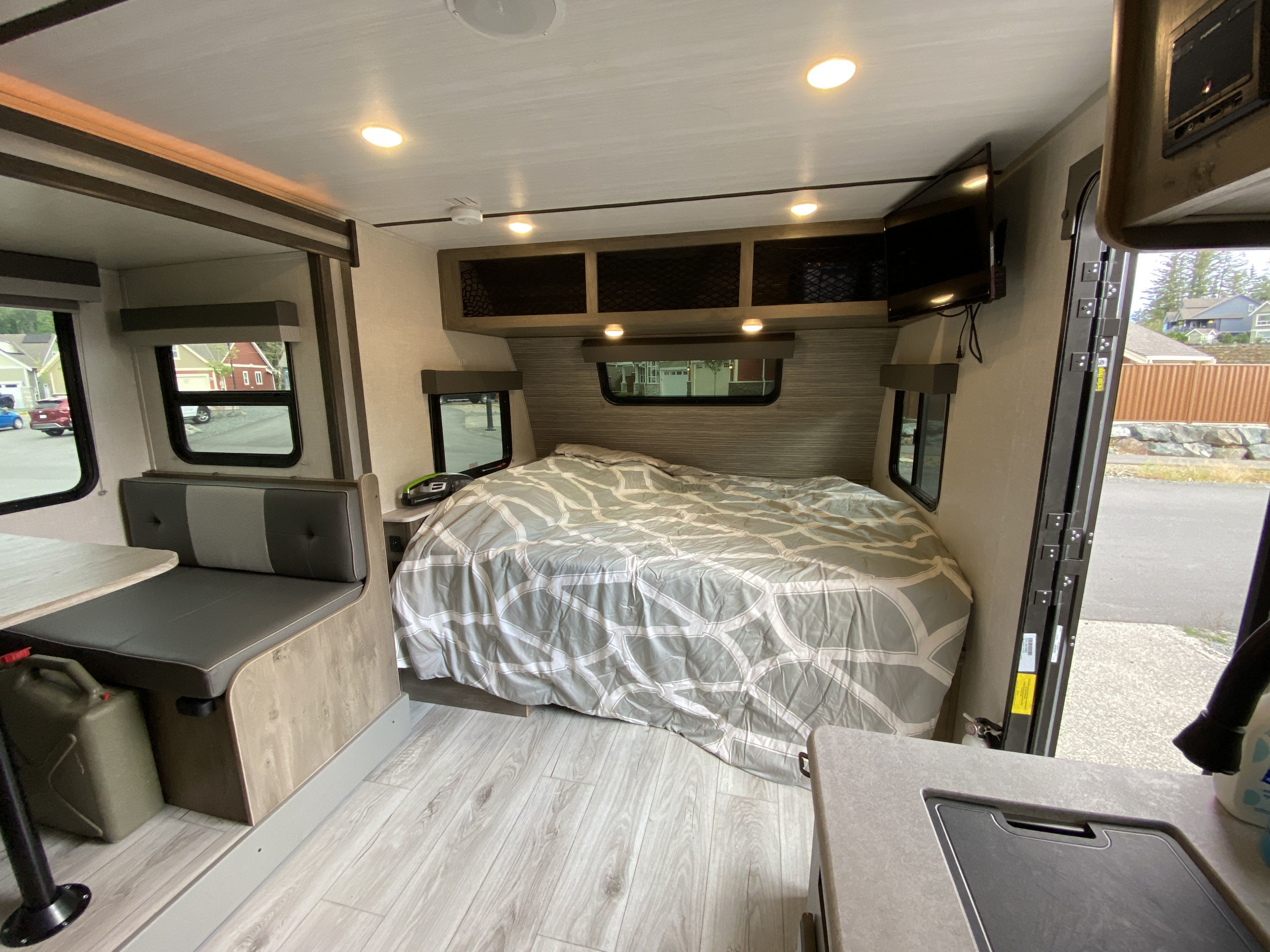 Bright RV rental interior showing a comfortable bed with grey patterned comforter, dinette, and storage.. Forest River Surveyor Legend 2022