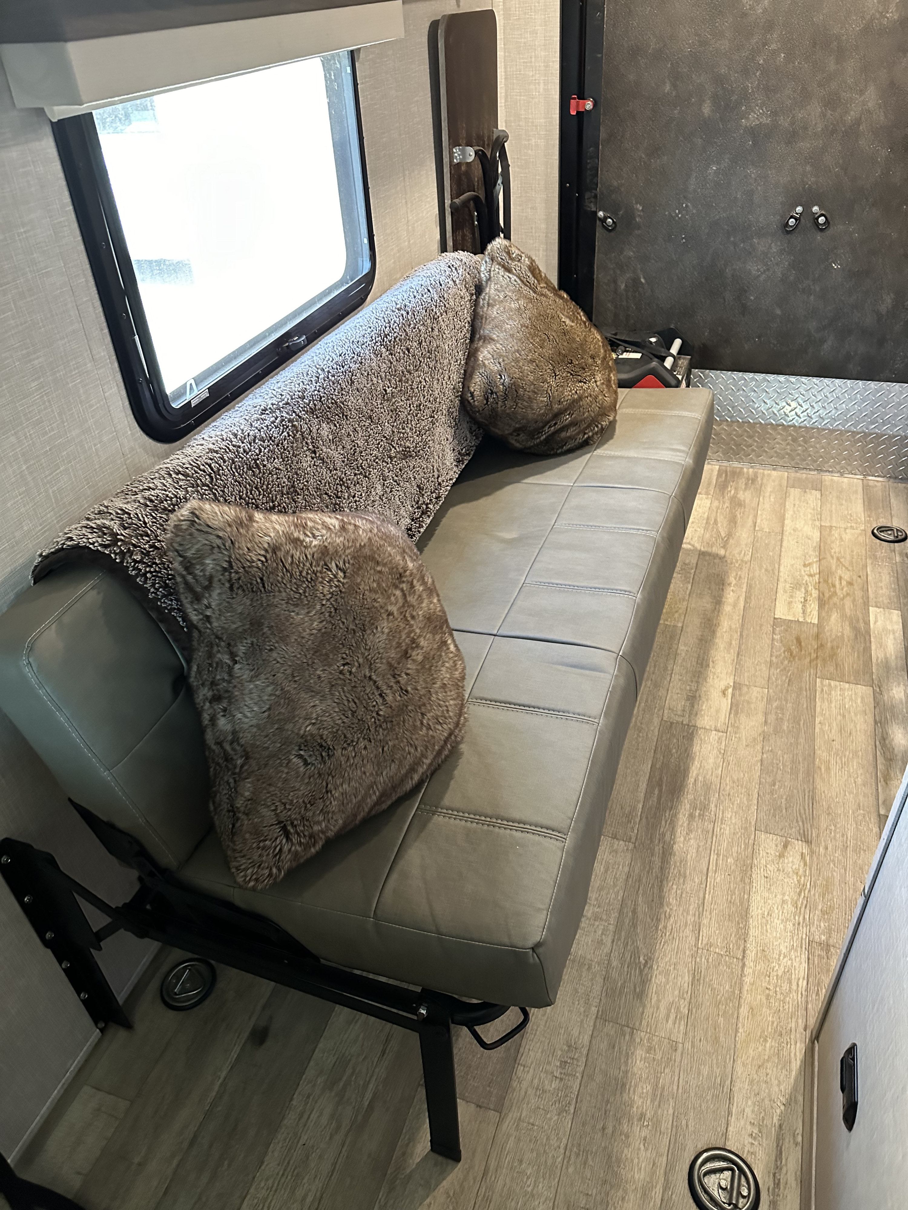 This RV rental interior shows a grey bench, cozy pillows, and a window. Durable flooring and tie-downs hint at a toy hauler design.. Forest River GeoPro 2022