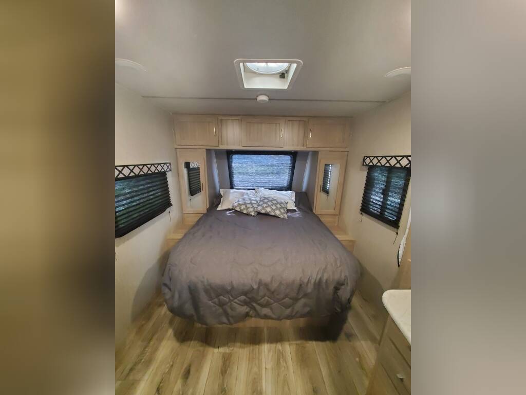 Cozy RV rental bedroom featuring a comfortable bed, overhead cabinets, and windows with blinds. Ideal for travel.. Coachmen Freedom Express 2020