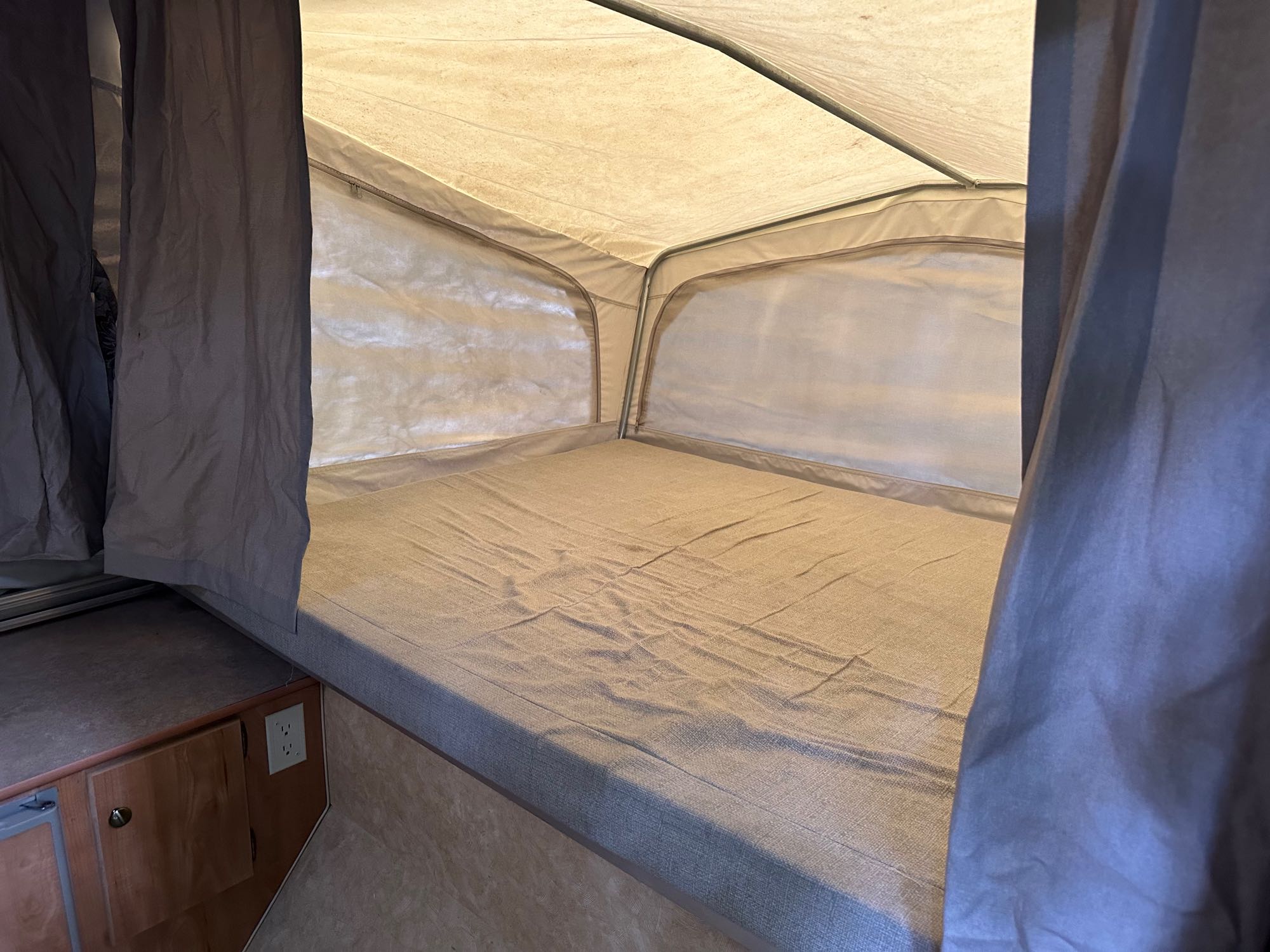 Inside an RV rental, a pop-up camper's comfortable bed with light-colored mattress and canvas tent walls.. Starcraft Starcraft Popup Trailer 2006