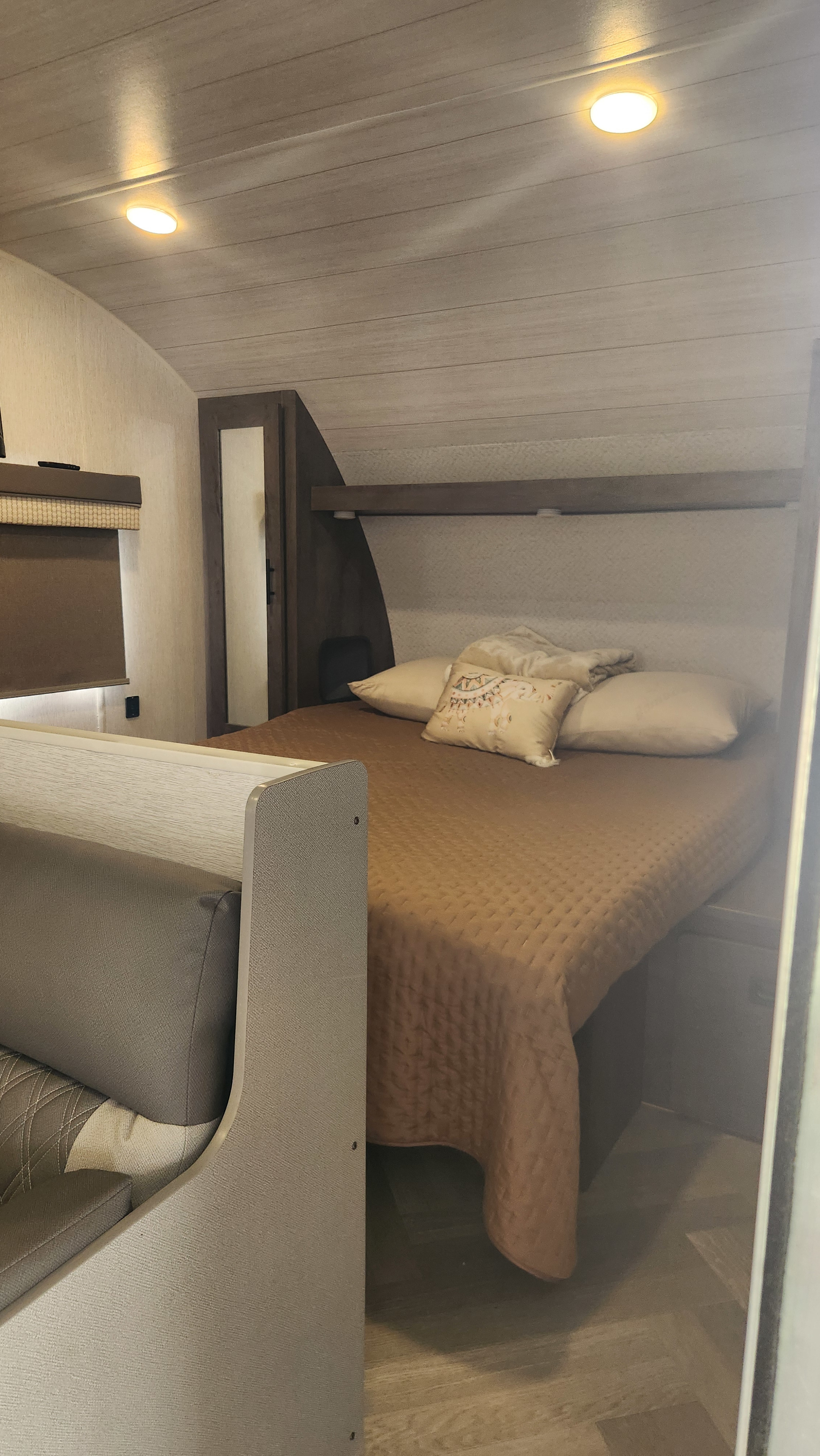 Compact bedroom and seating area in an RV rental, featuring a comfortable bed, built-in storage, and bright interior lighting.. Forest River Wildwood X-Lite 2022