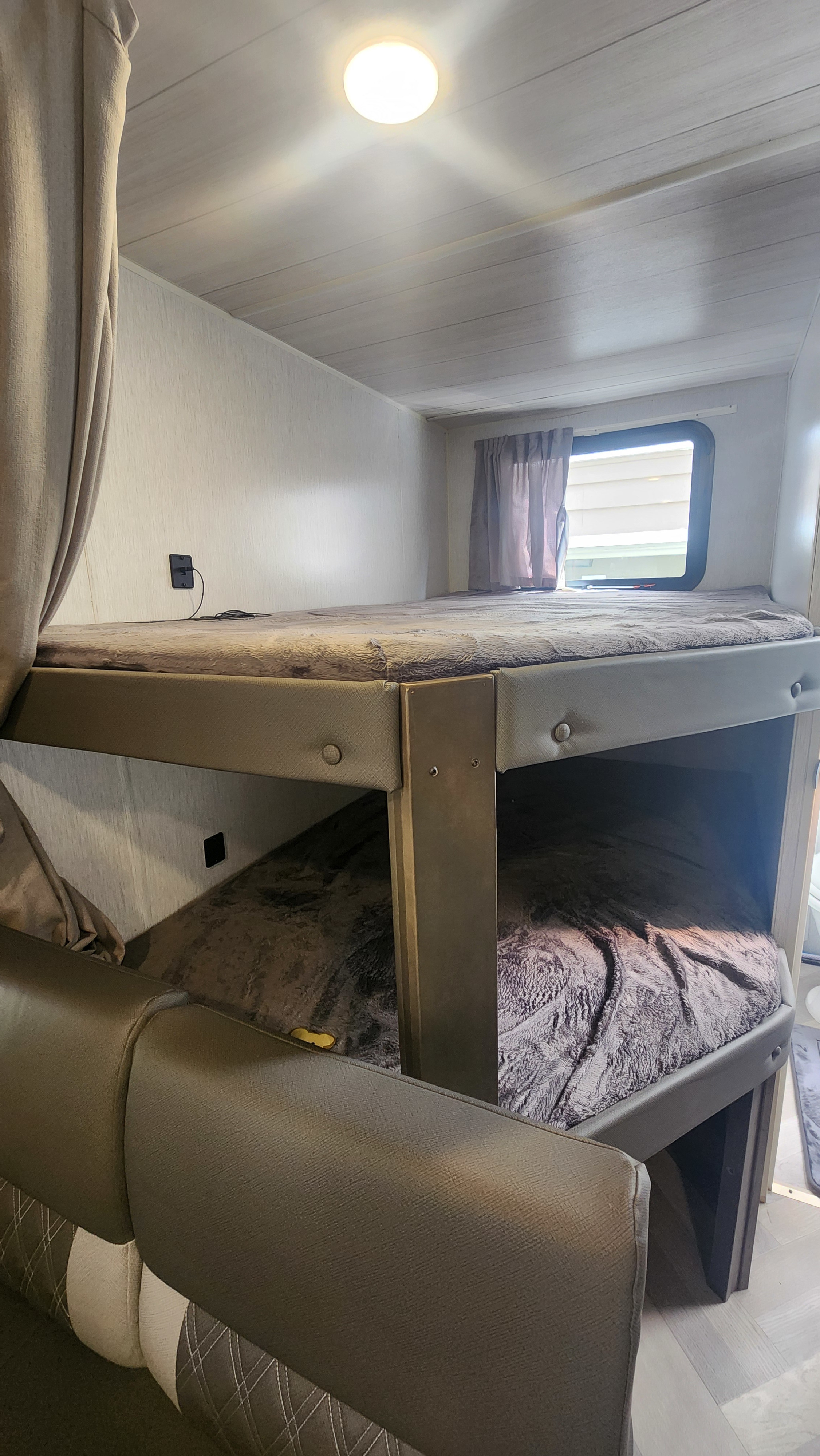 Cozy bunk beds inside an RV rental. Features a window, ceiling light, and charging port, ideal for travel.. Forest River Wildwood X-Lite 2022