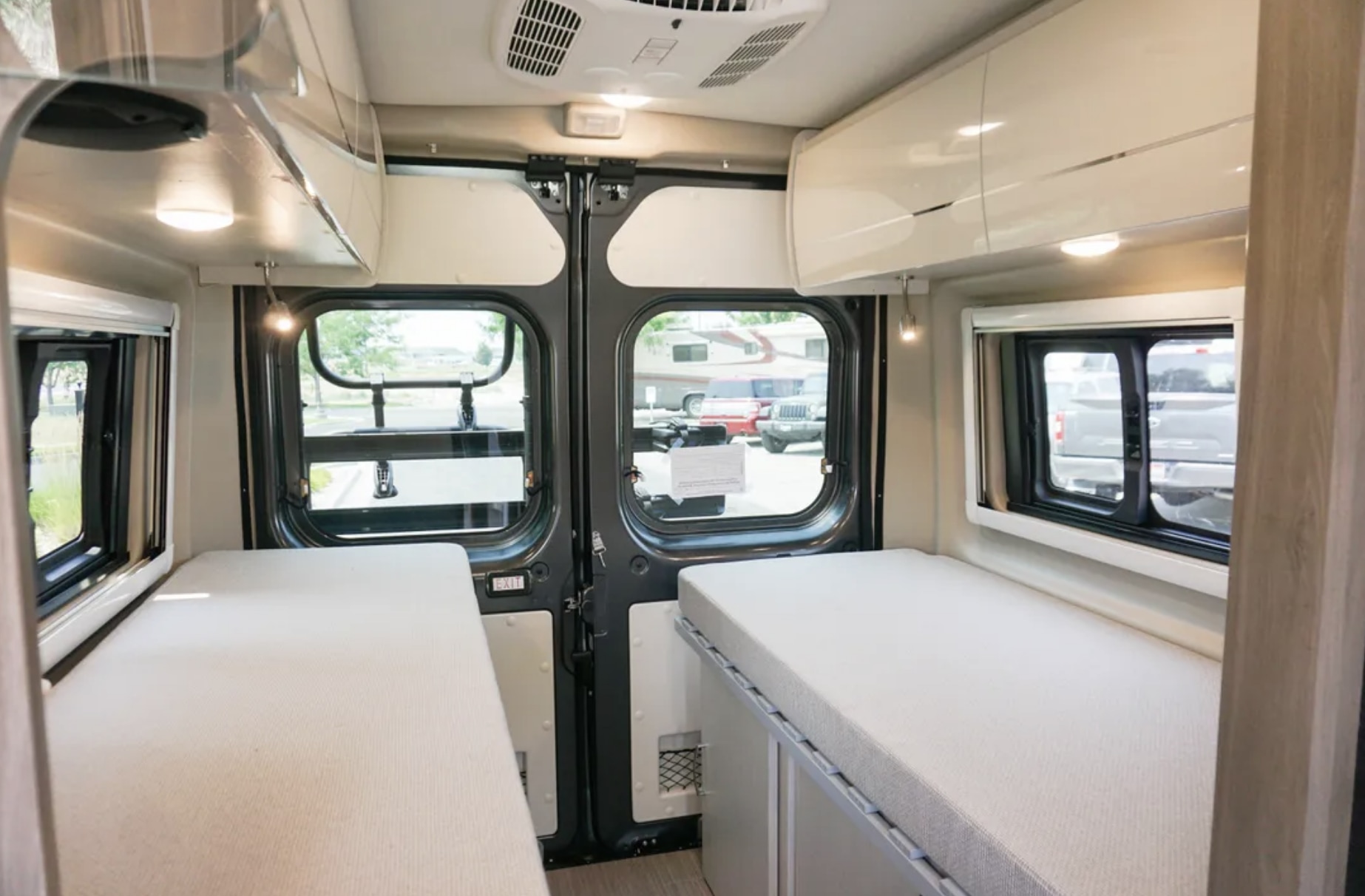 Spacious RV rental interior with dual single beds, overhead storage, and large rear windows for comfort and views.. Thor Tellaro 2022