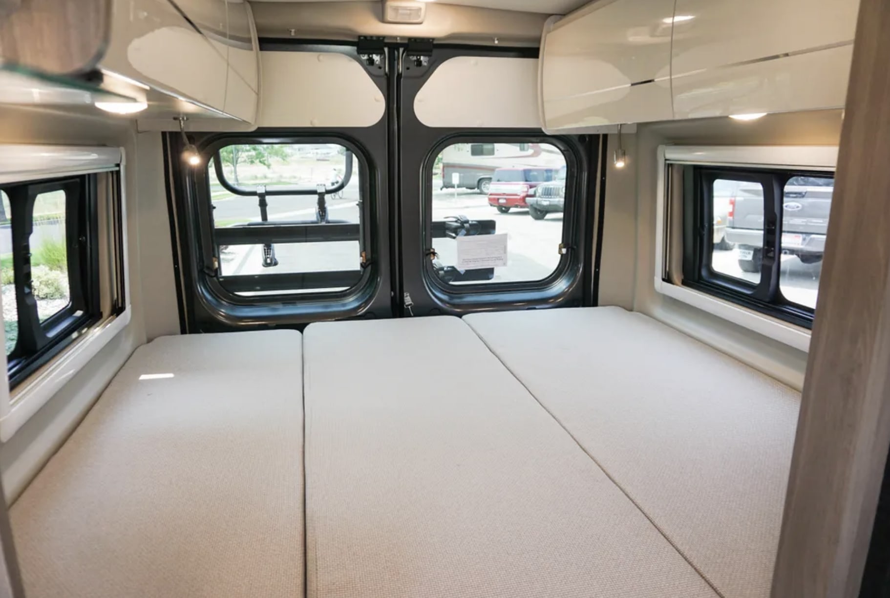 RV rental camper van interior. Spacious sleeping area with three mattress sections, large rear windows, and overhead storage.. Thor Tellaro 2022