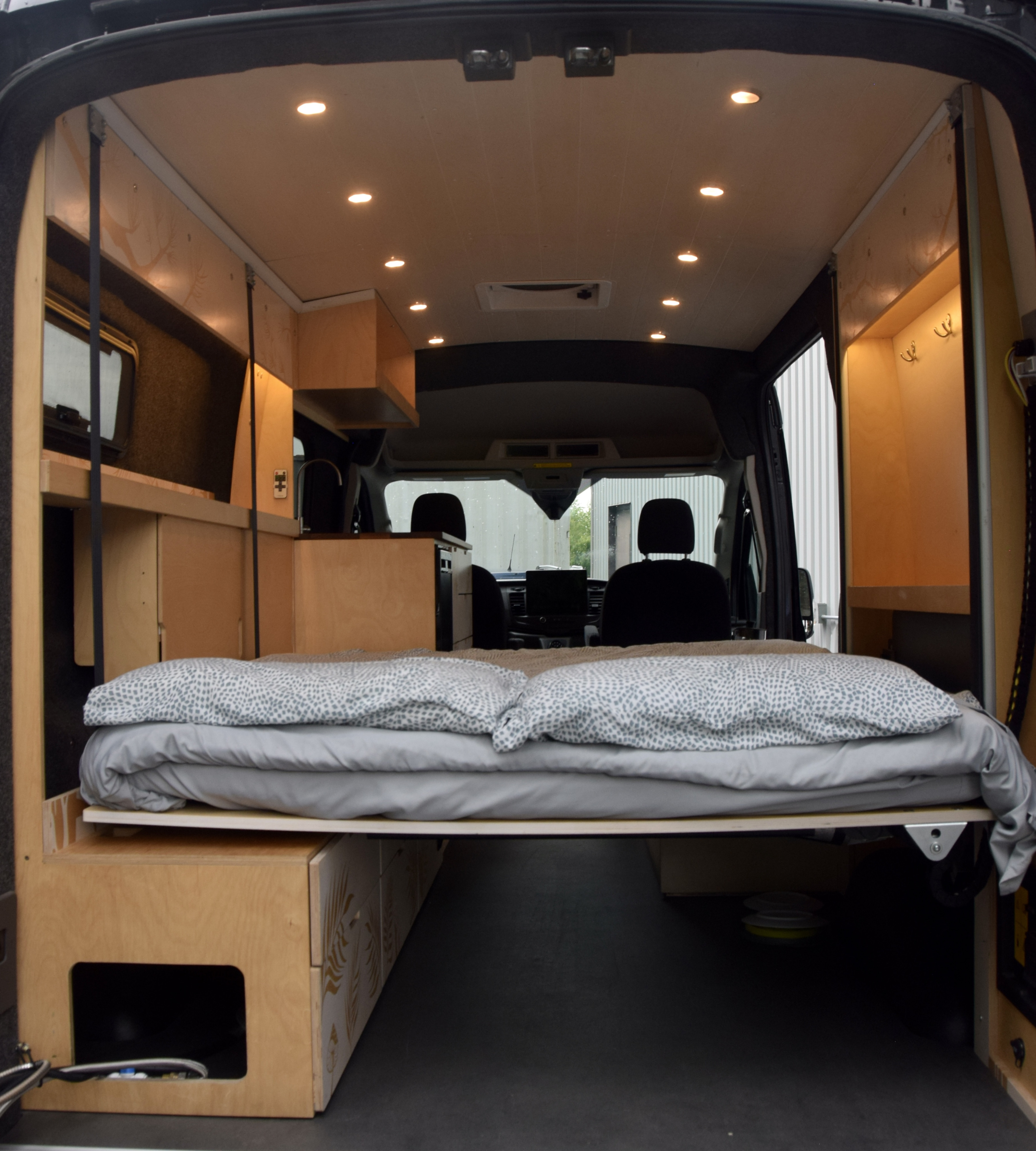This RV rental camper van features a cozy bed, custom wood interior, and ceiling lights, ready for adventure.. Ford Electric-TRANSIT 2022