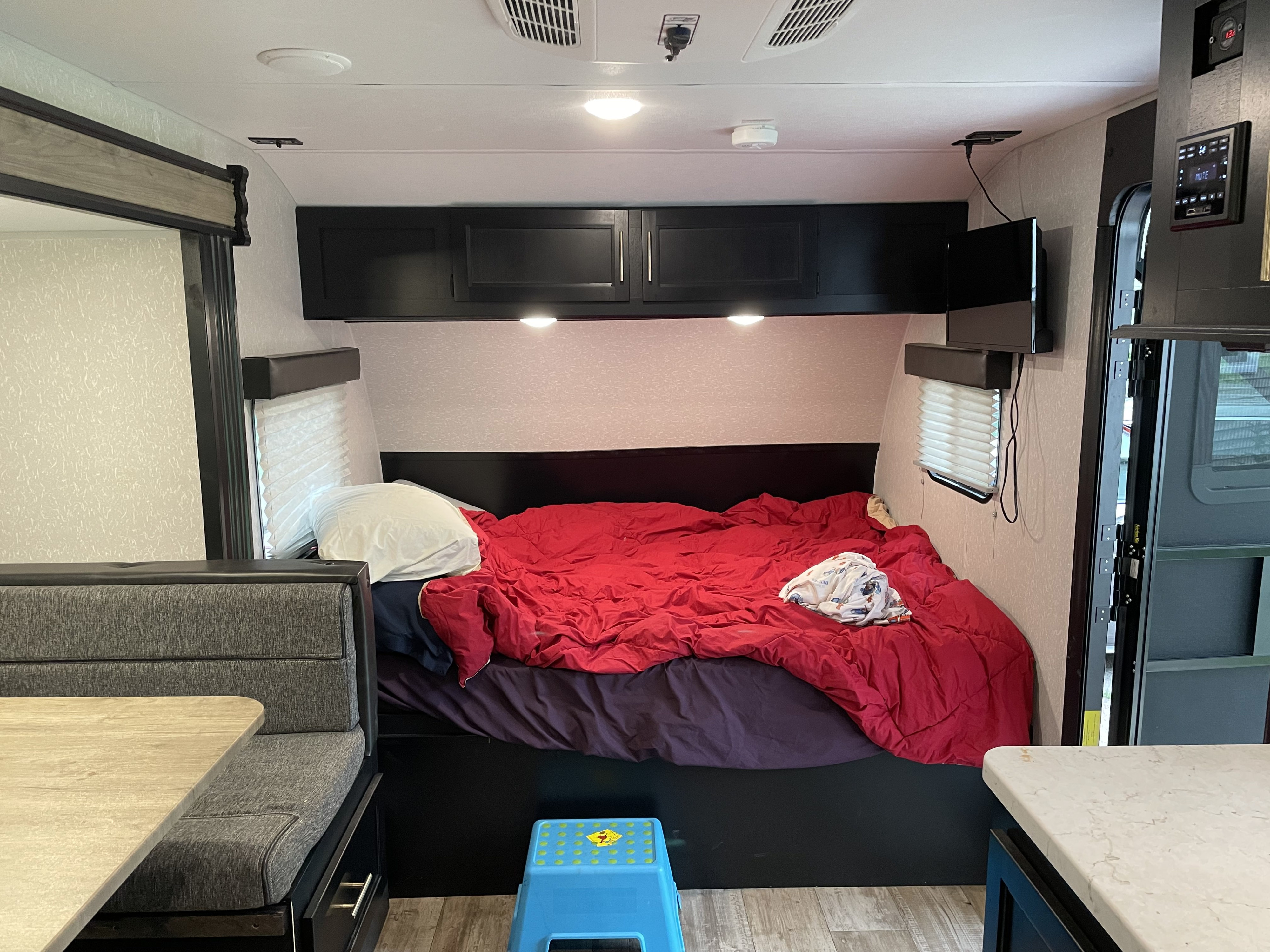 Inside a compact RV rental, featuring a comfortable bed with a red comforter and a small dinette area.. Forest River Cherokee Wolf Pup 2022