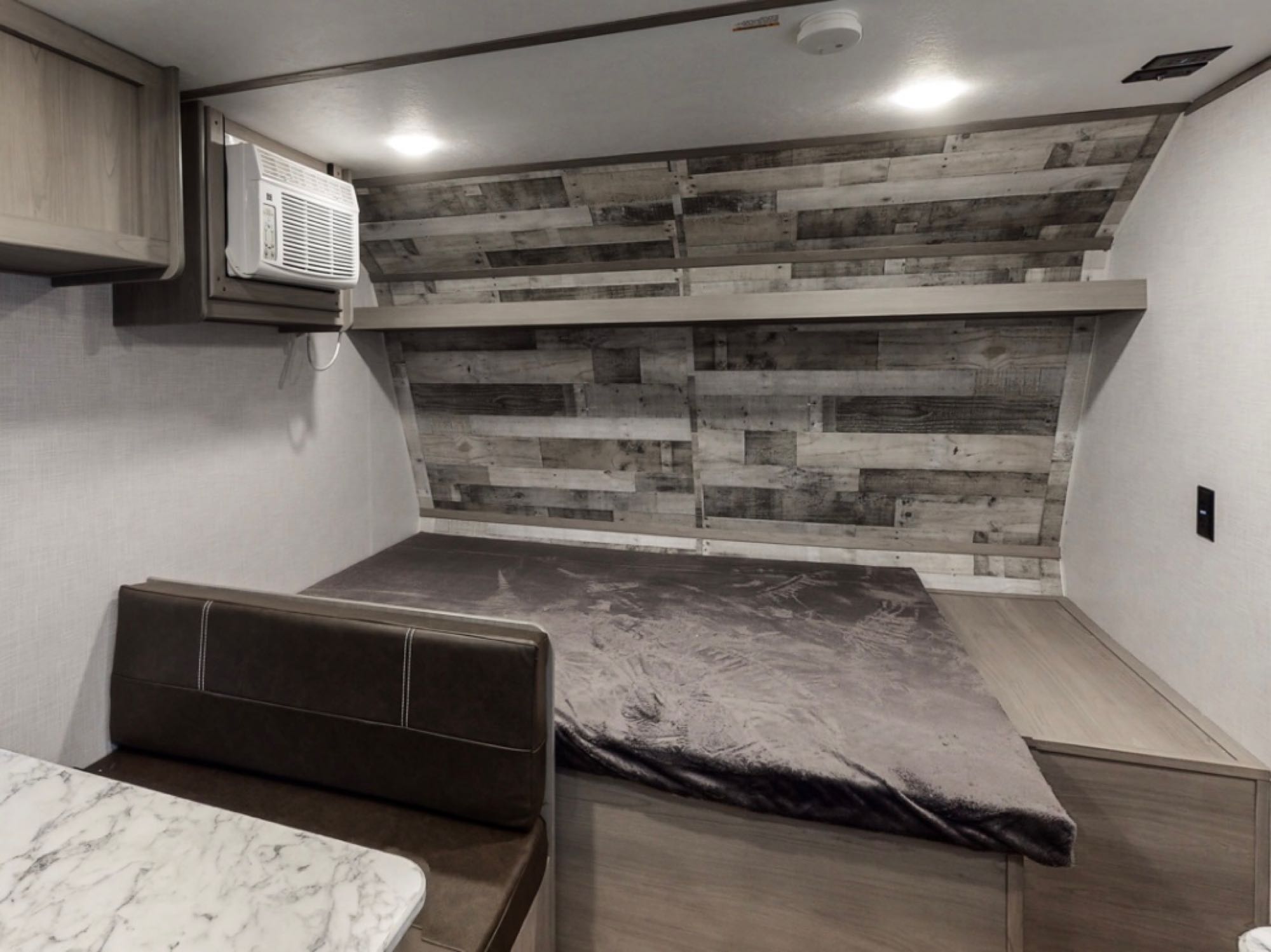 This RV rental features a cozy bedroom with a bed, wood-paneled wall, AC, and dinette seating. Ready for adventure!. Dutchmen Coleman Lantern LT 17B 2024